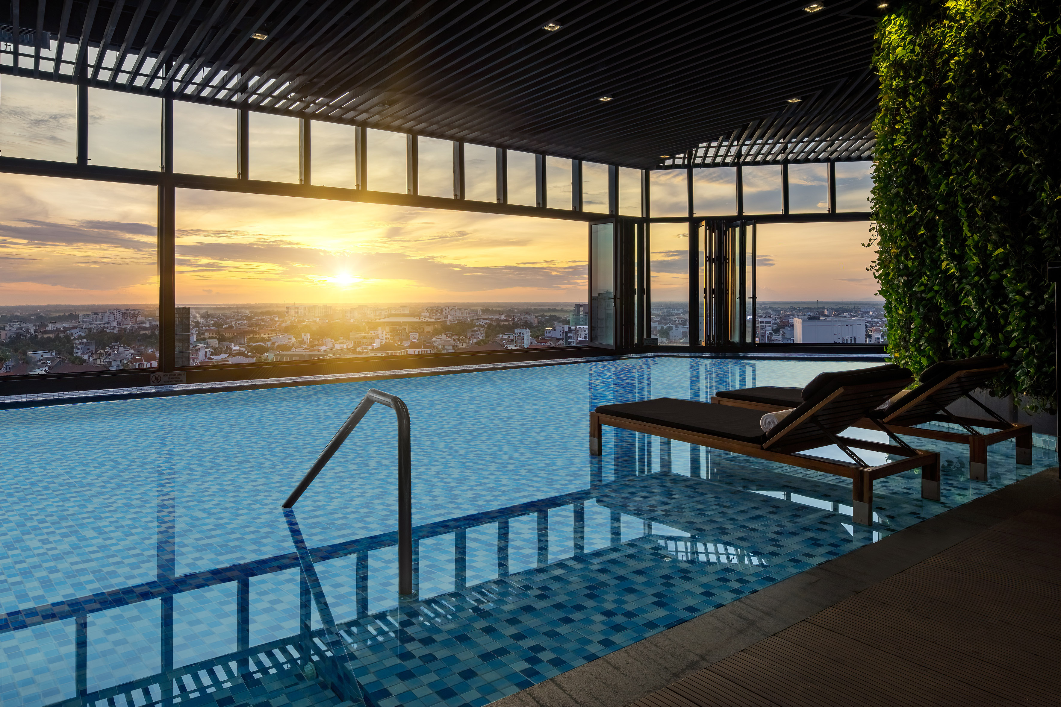 Rooftop infinity pool with sunset city skyline view, modern design, and lounge chairs.