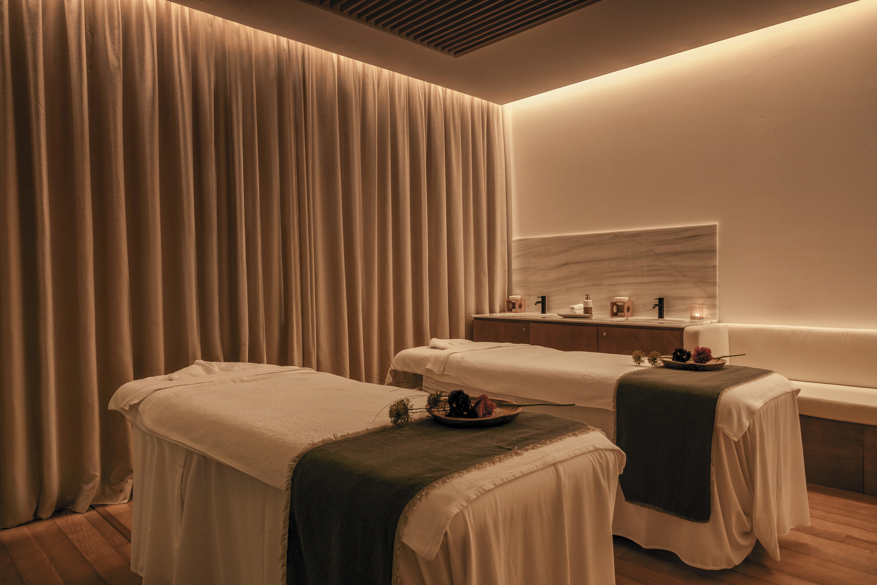 Luxurious spa treatment room with two massage tables and warm ambient lighting.