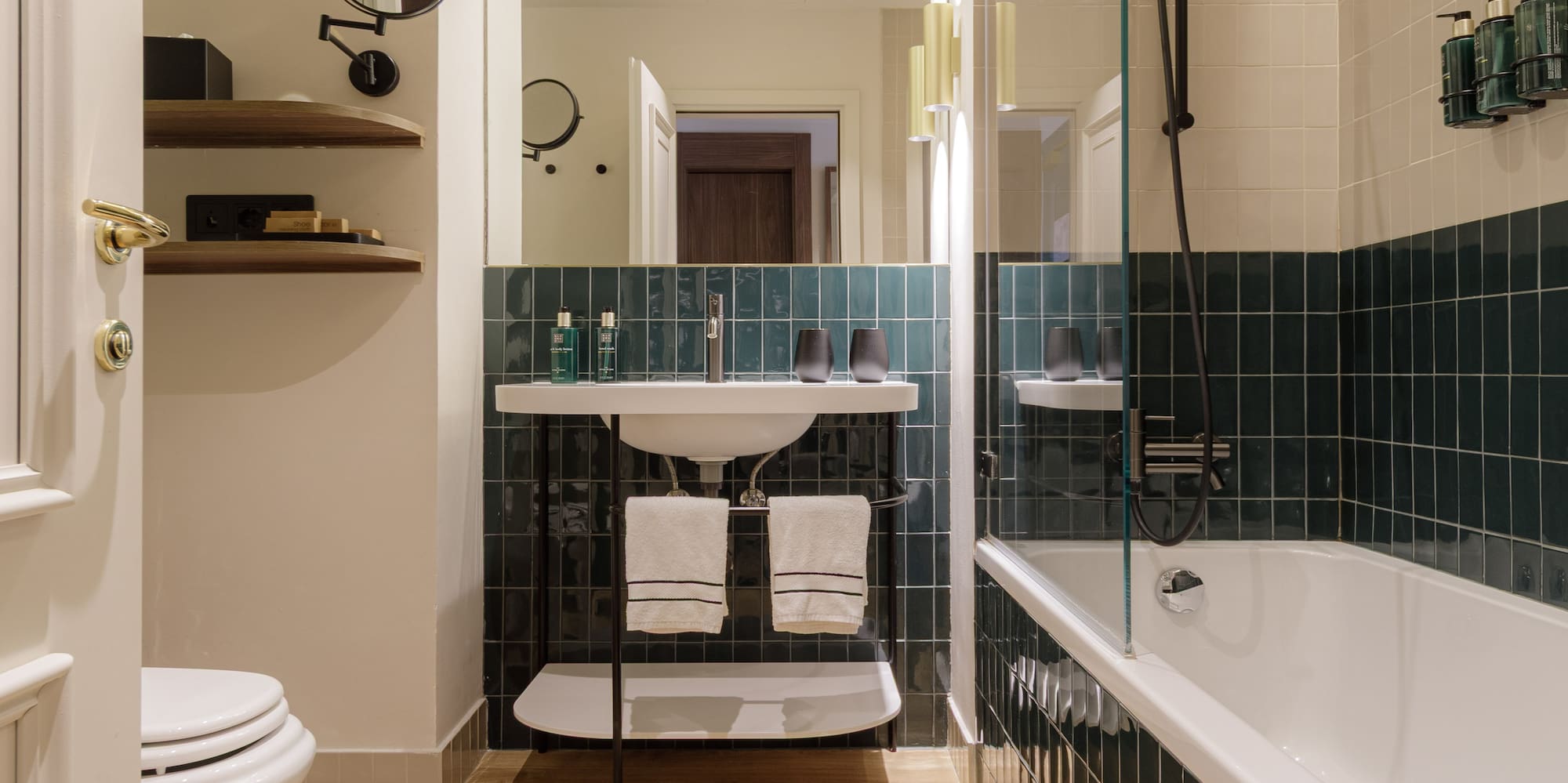 Modern bathroom with wood floor, green tiled walls, white tub, toilet, and sink.