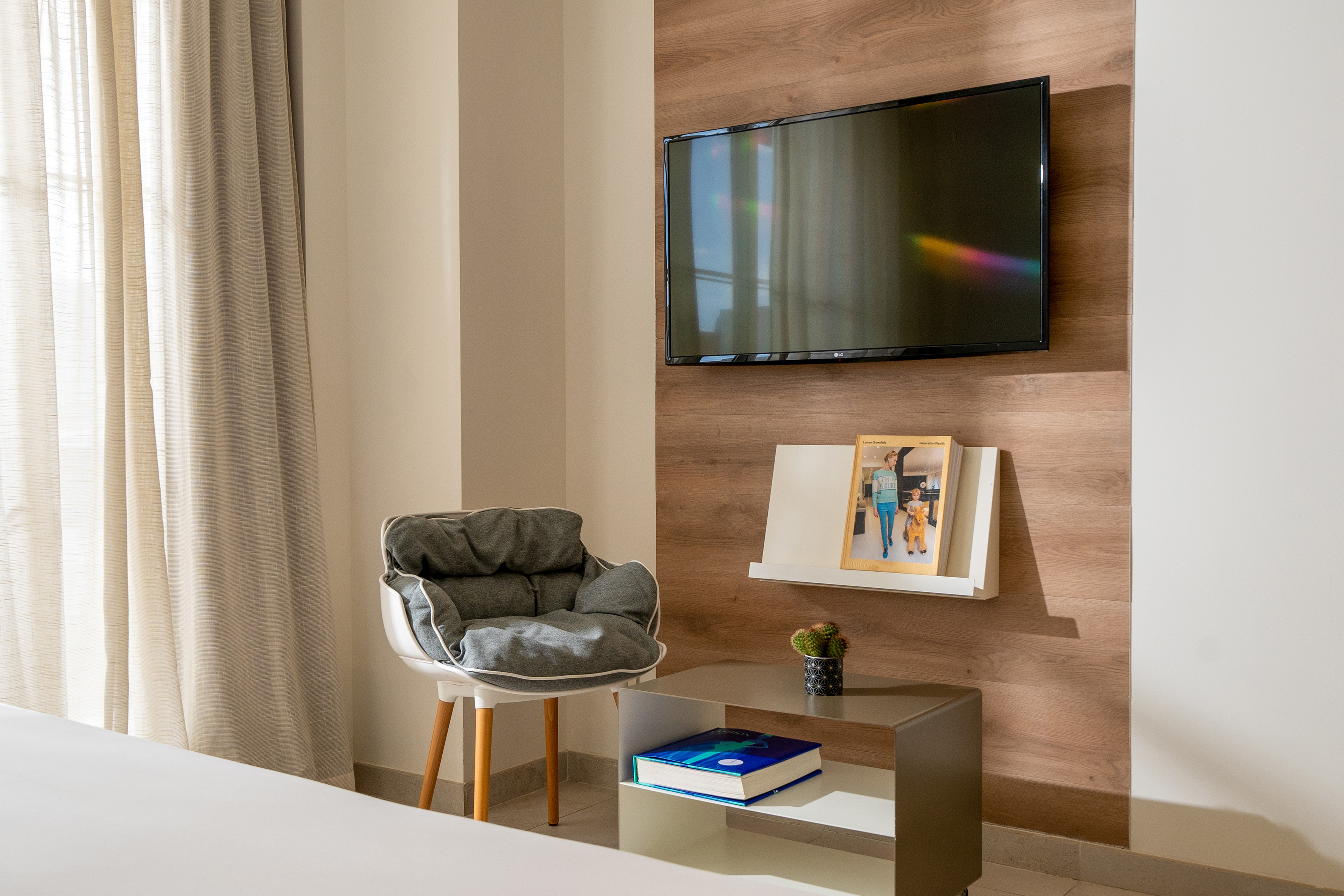 Contemporary hotel room with wall TV, armchair, and wood paneling.