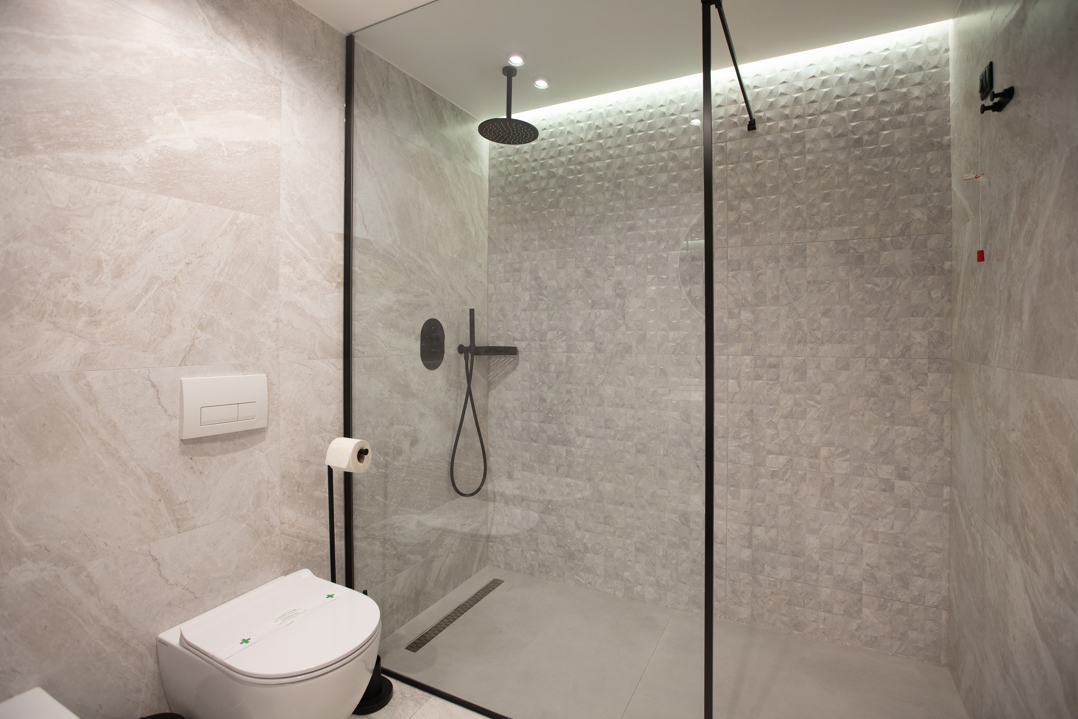 Modern gray tiled bathroom with walk-in shower, rain showerhead, and toilet.