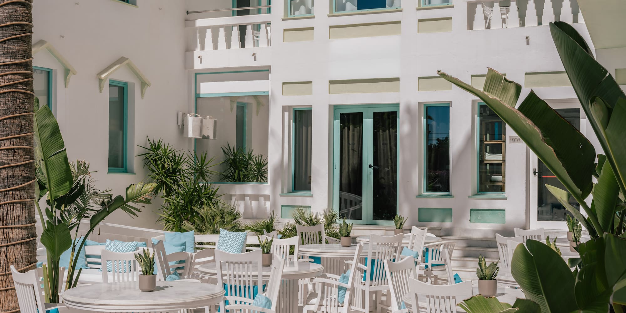 White resort patio, turquoise windows, al fresco dining, tropical plants.
