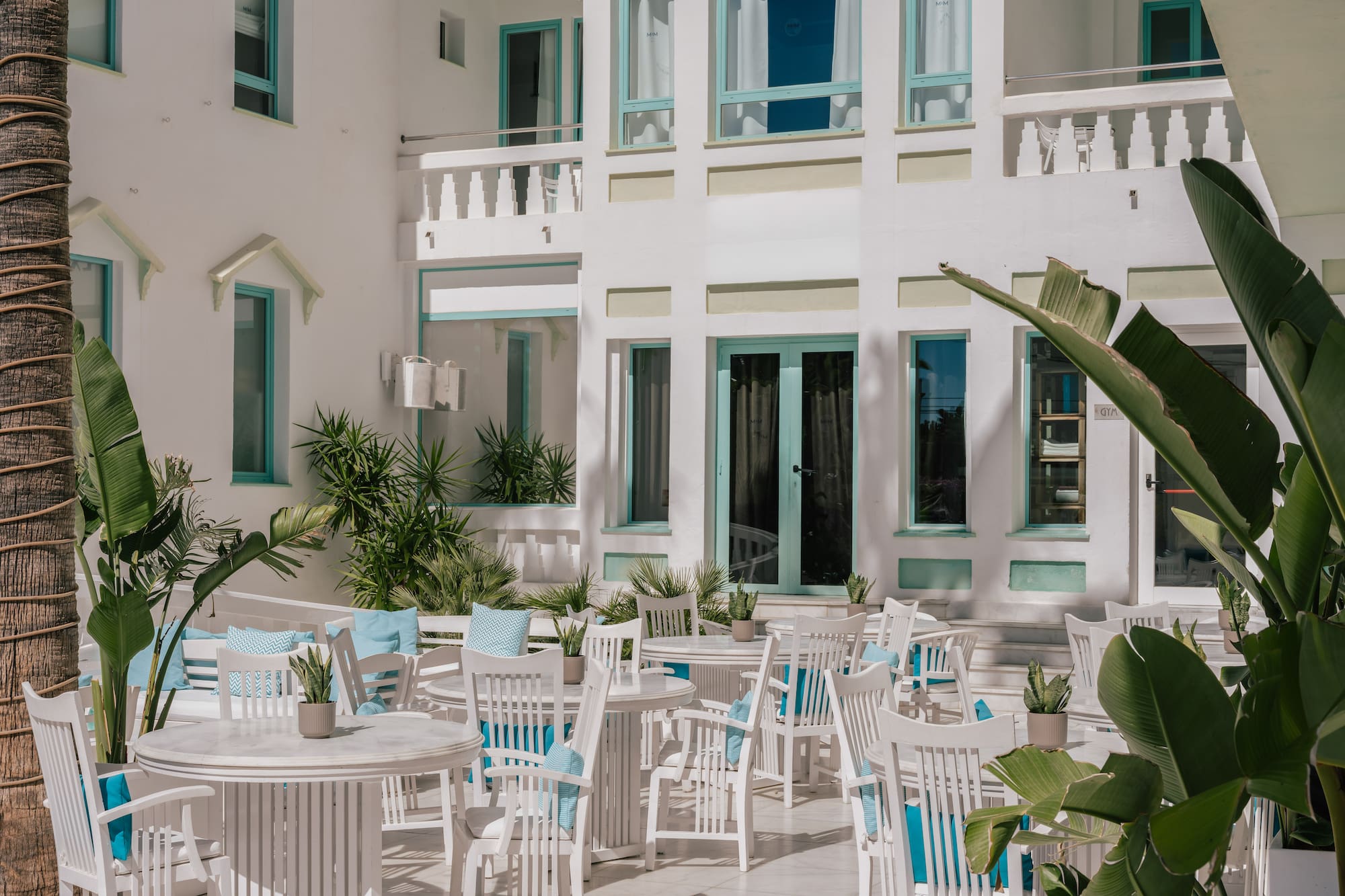 White Mediterranean resort patio with blue seating and lush tropical plants.
