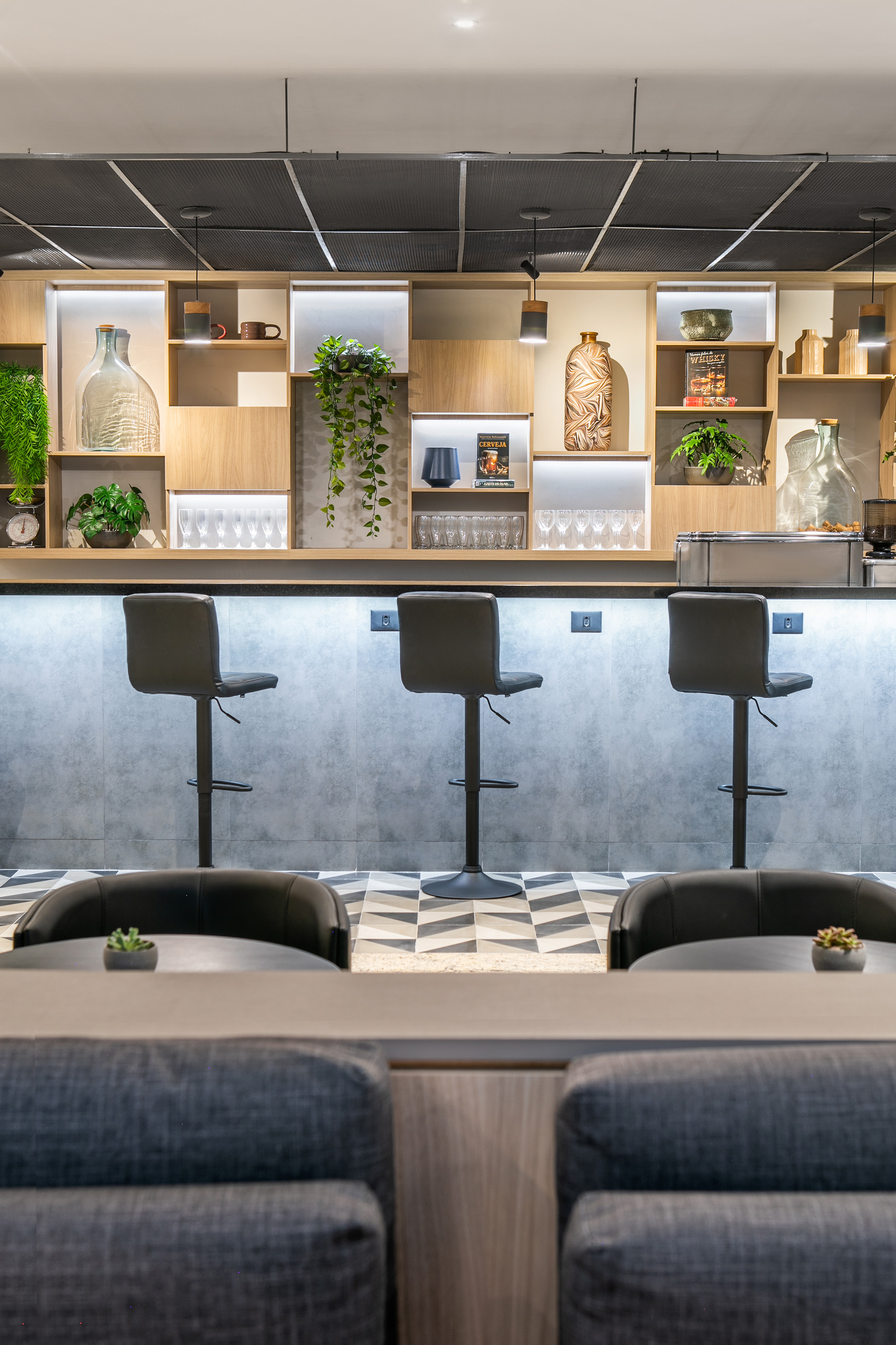 Contemporary bar counter with lit display shelves, plants, and geometric floor.