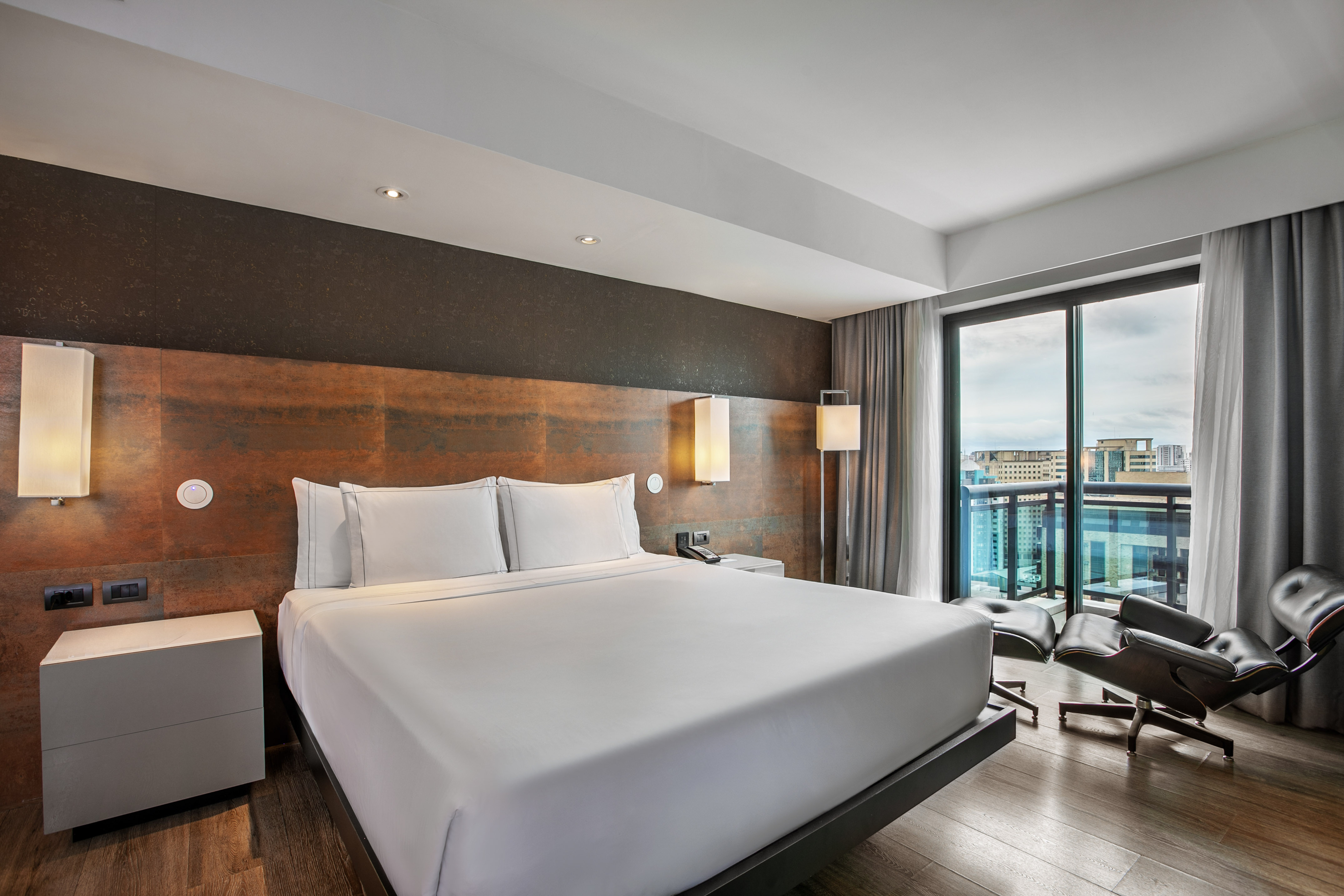 Quarto de hotel moderno com cama king-size, cabeceira rústica e grande janela. - Grand Premium com Varanda - Meliá Ibirapuera, São Paulo
