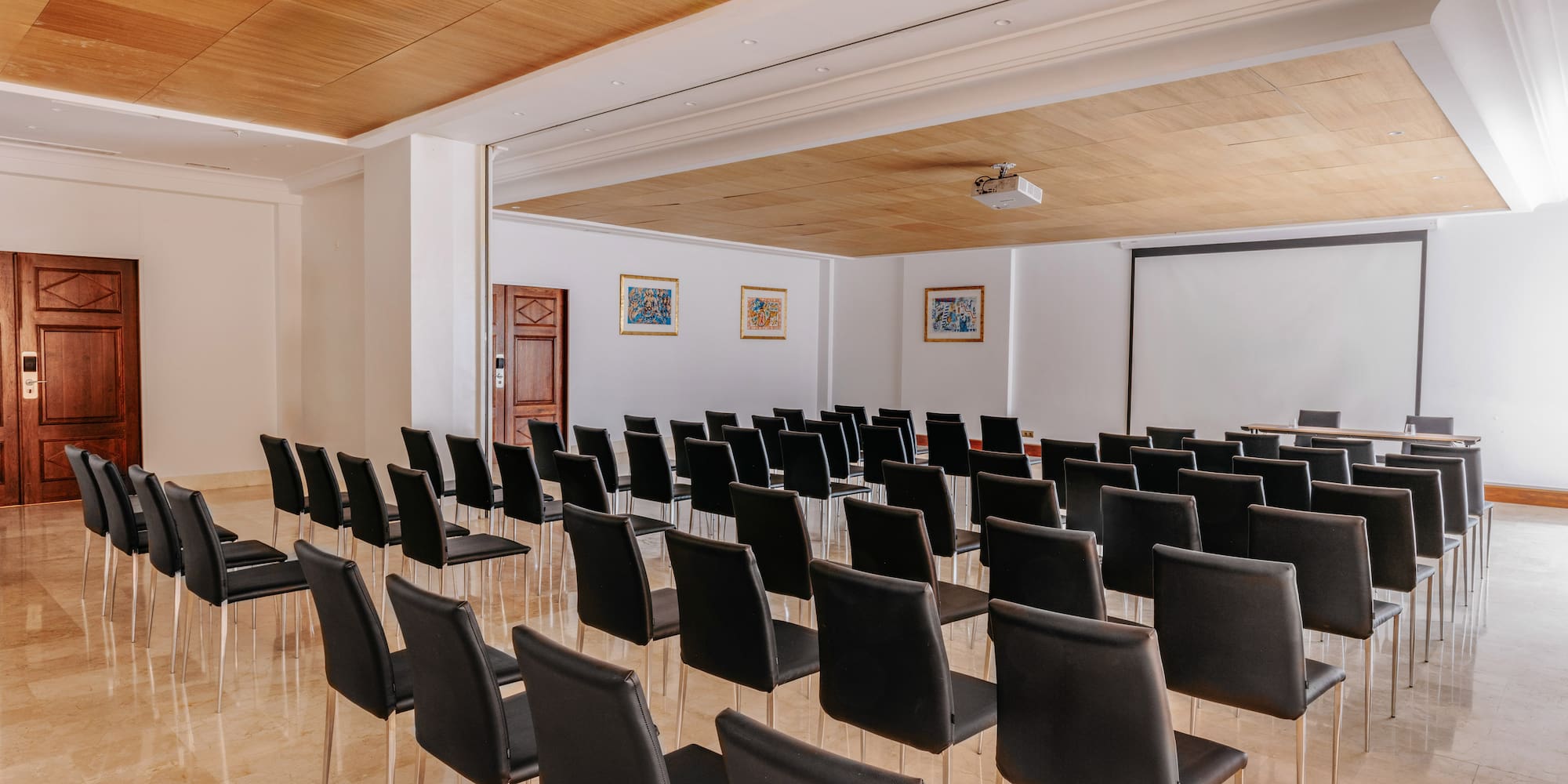 Well-lit empty meeting room with black chairs, projector, and large screen.