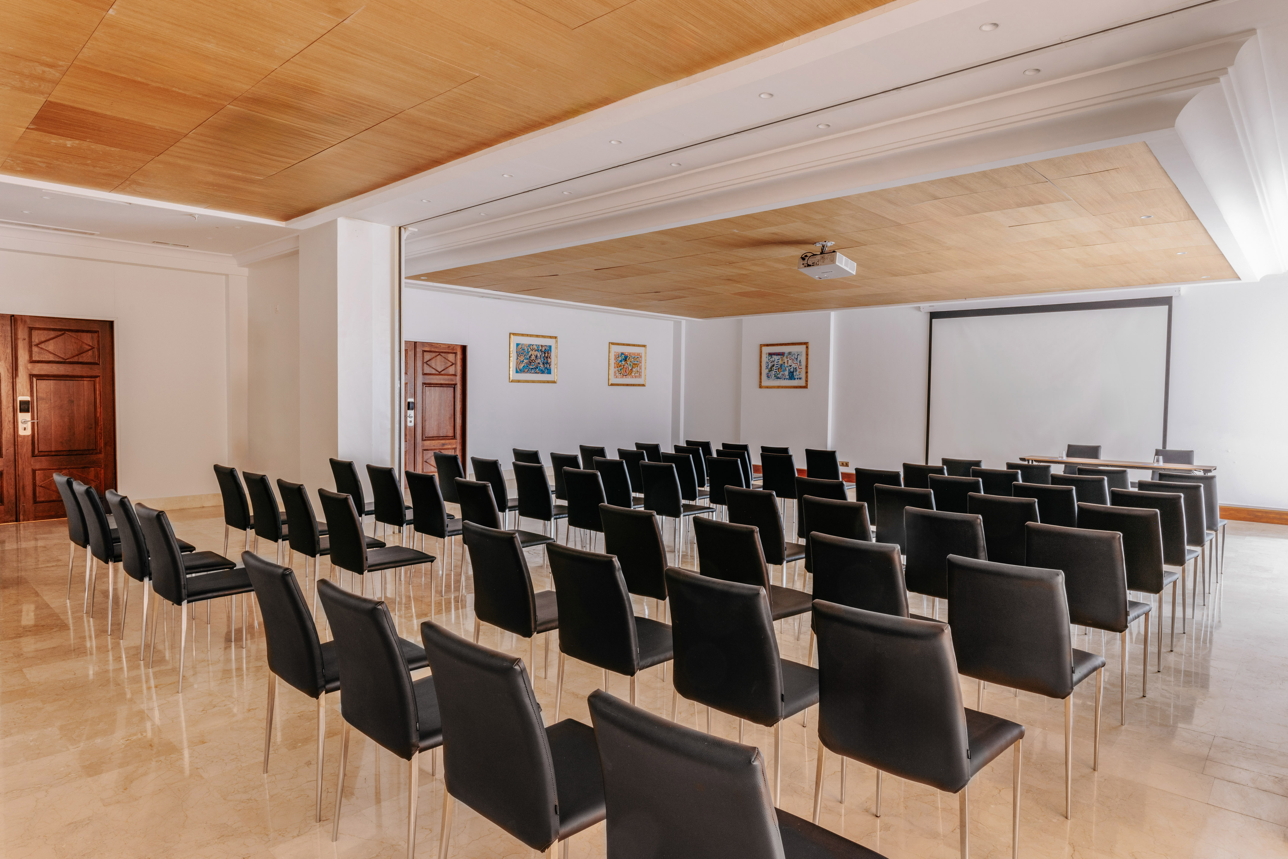 Well-lit empty meeting room with black chairs, projector, and large screen.