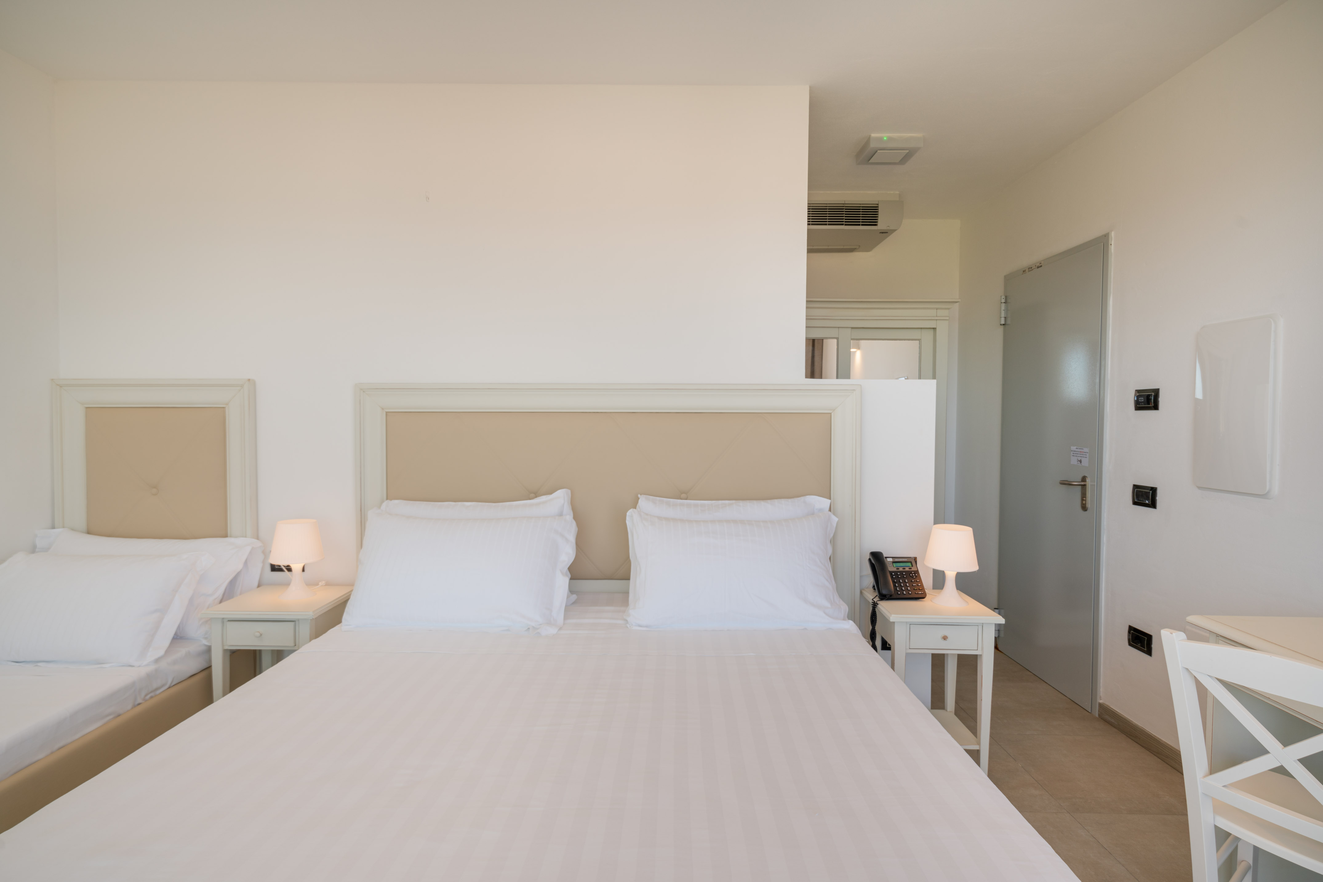 Bright guest room with double and twin beds, white linens, and modern decor.