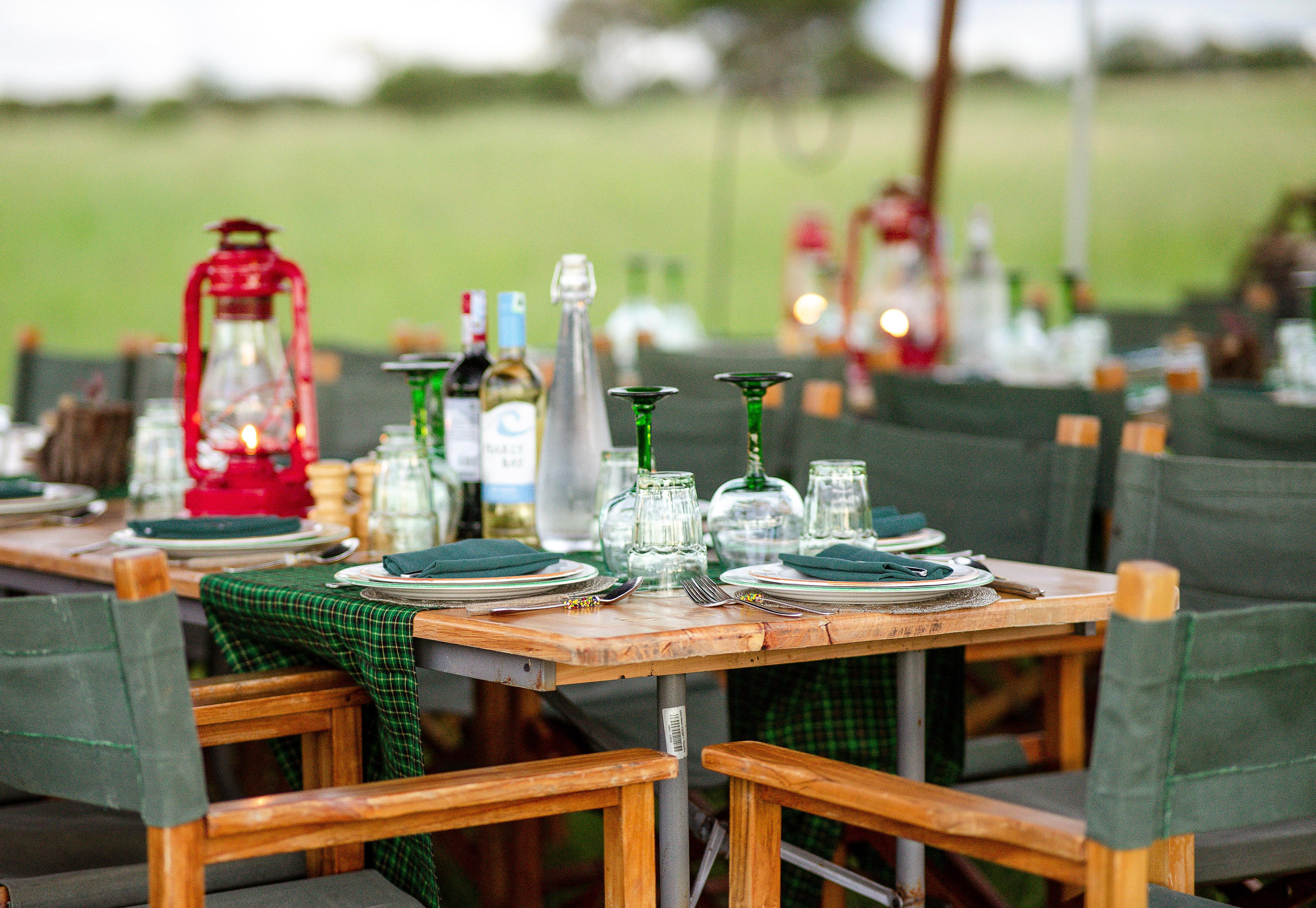 Outdoor dining table set with red lanterns, wine, and green safari chairs.