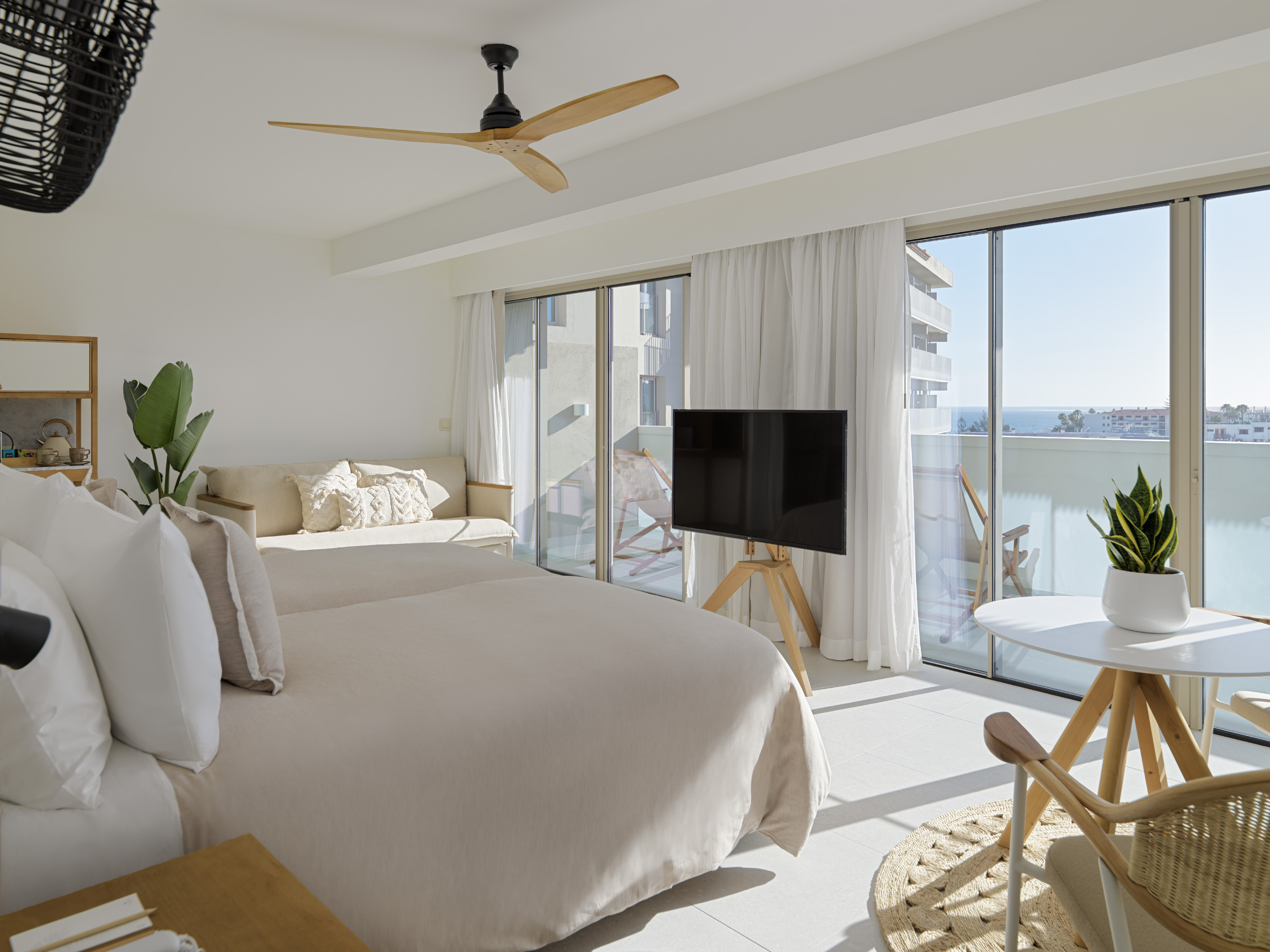 Modern resort bedroom with sea view balcony, large bed, TV, and ceiling fan.