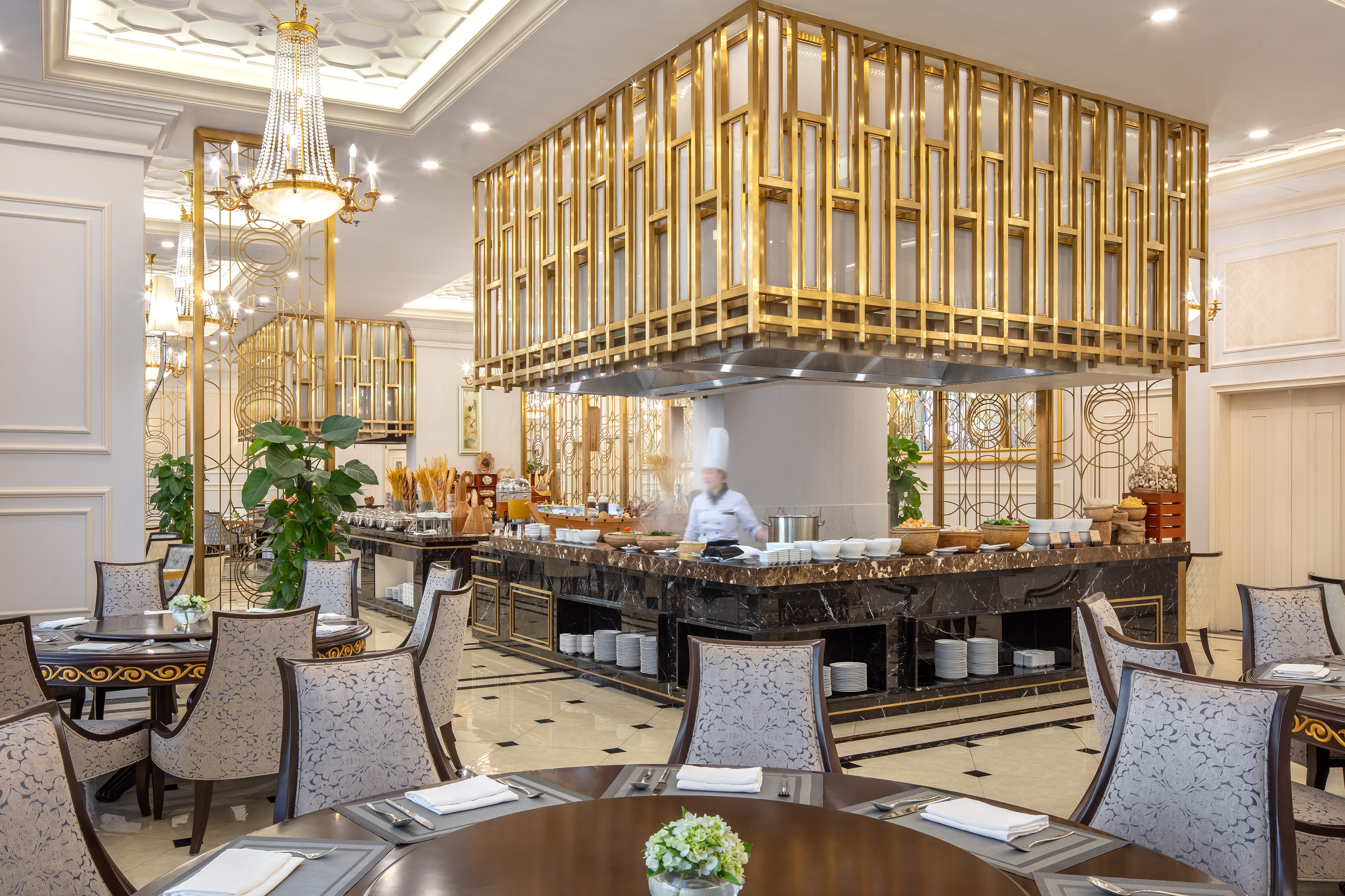 Elegant hotel buffet with chef, gold decor, and marble serving station.