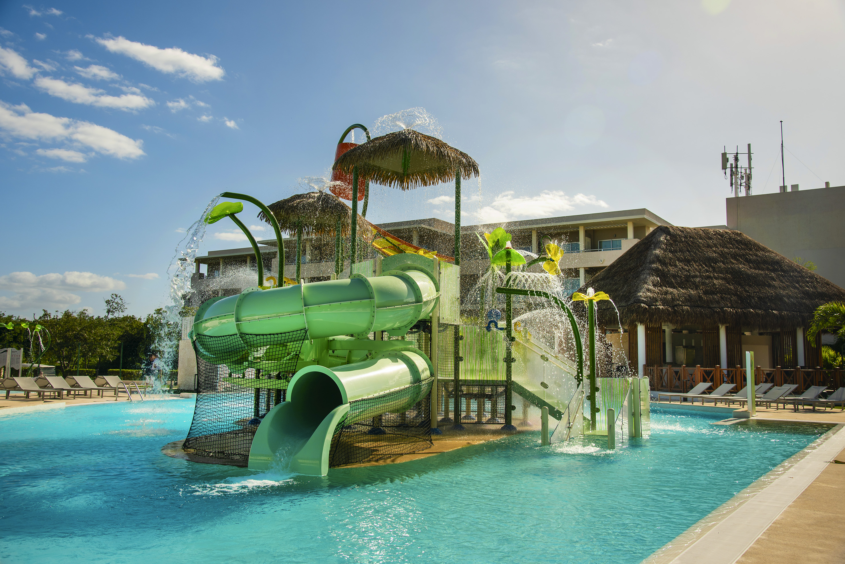 Tropical resort water park with bright green slides, splash features, and pool.