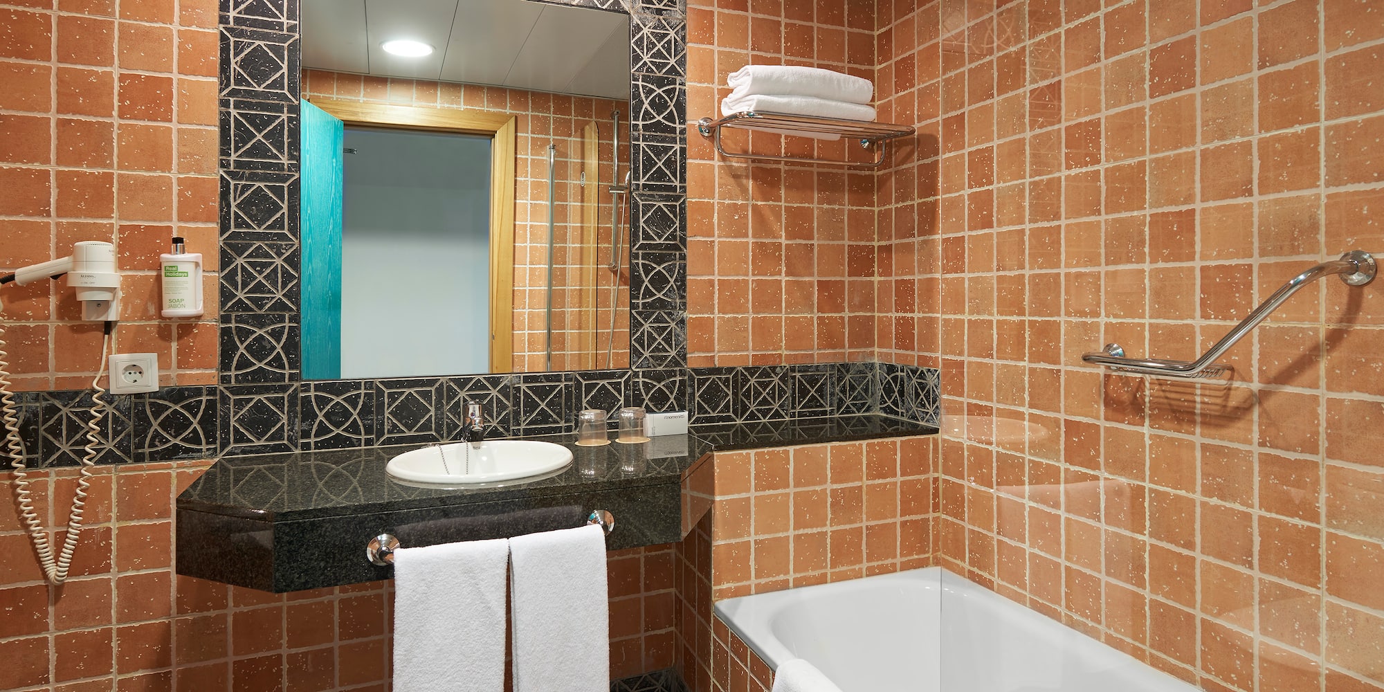 Terracotta tiled hotel bathroom with white bathtub, vanity, and mirror.