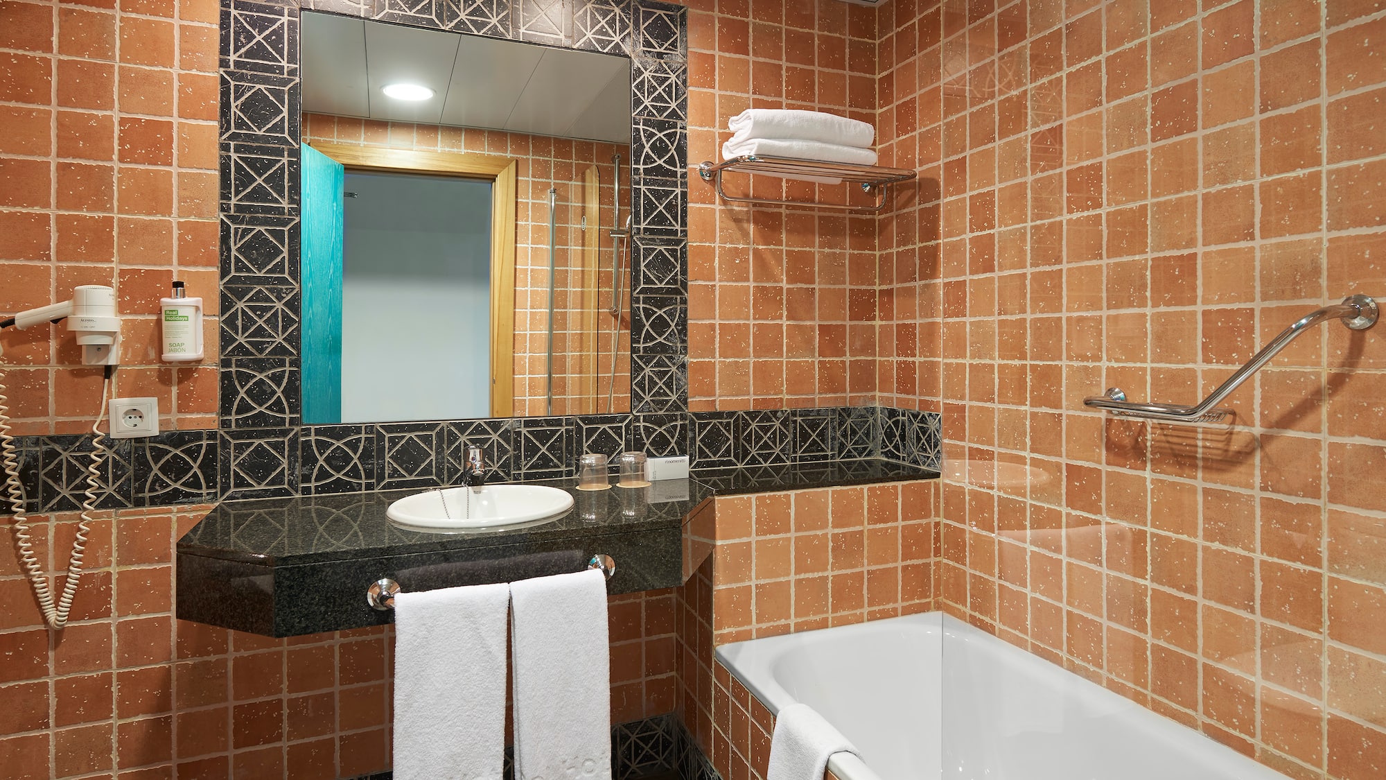 Terracotta tiled hotel bathroom with white bathtub, vanity, and mirror.