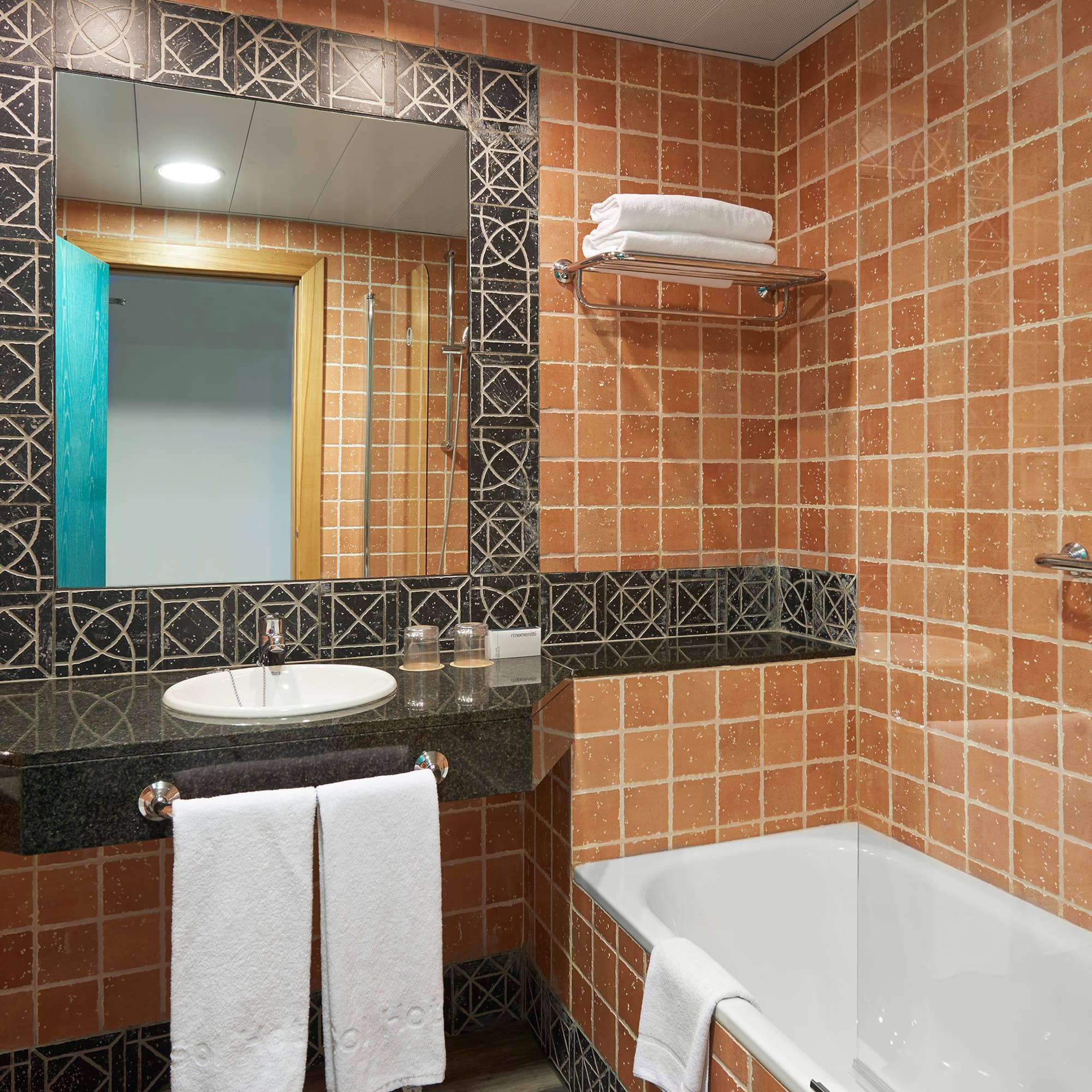 Terracotta tiled hotel bathroom with white bathtub, vanity, and mirror.