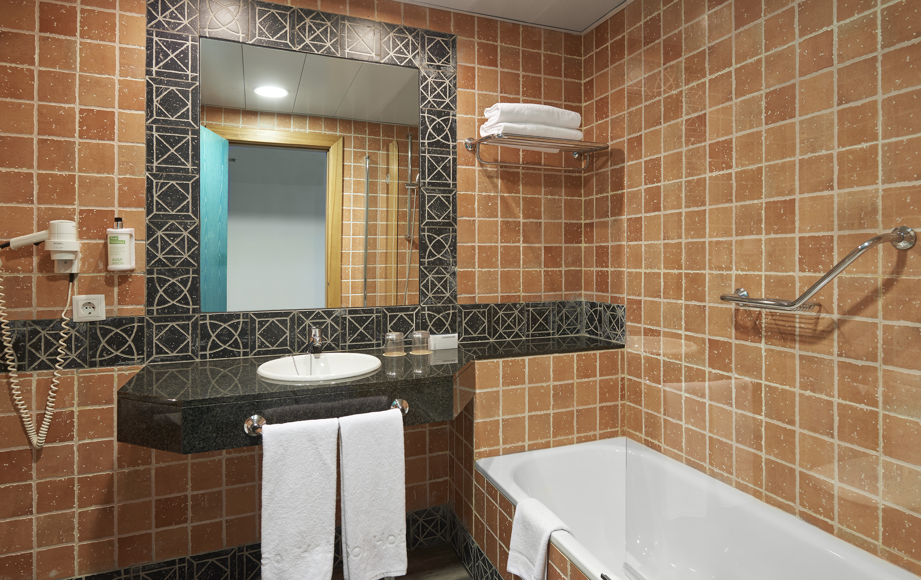 Terracotta tiled hotel bathroom with white bathtub, vanity, and mirror.