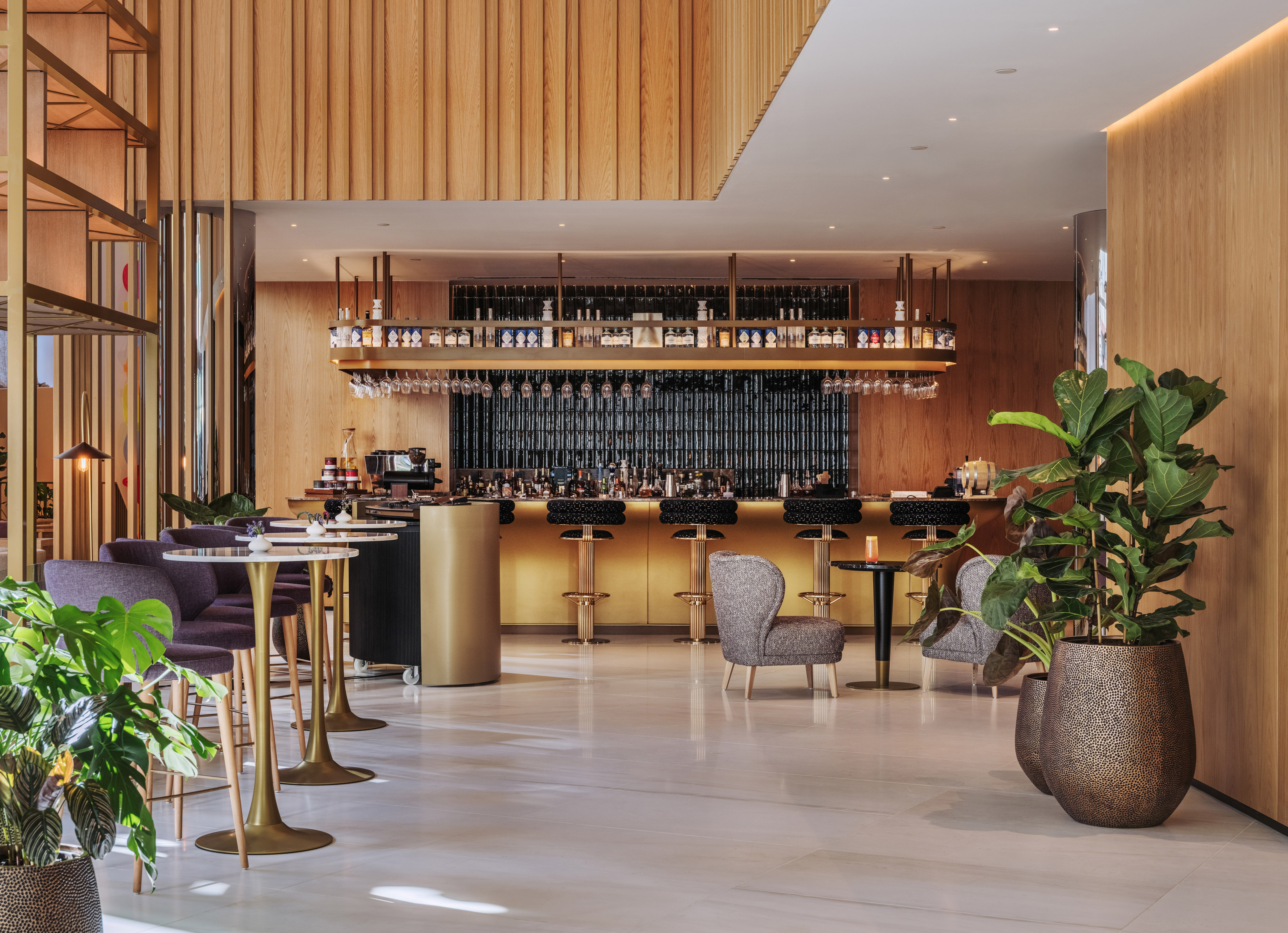 Modern luxury bar with golden counter, wood paneling, marble floor, and plants.