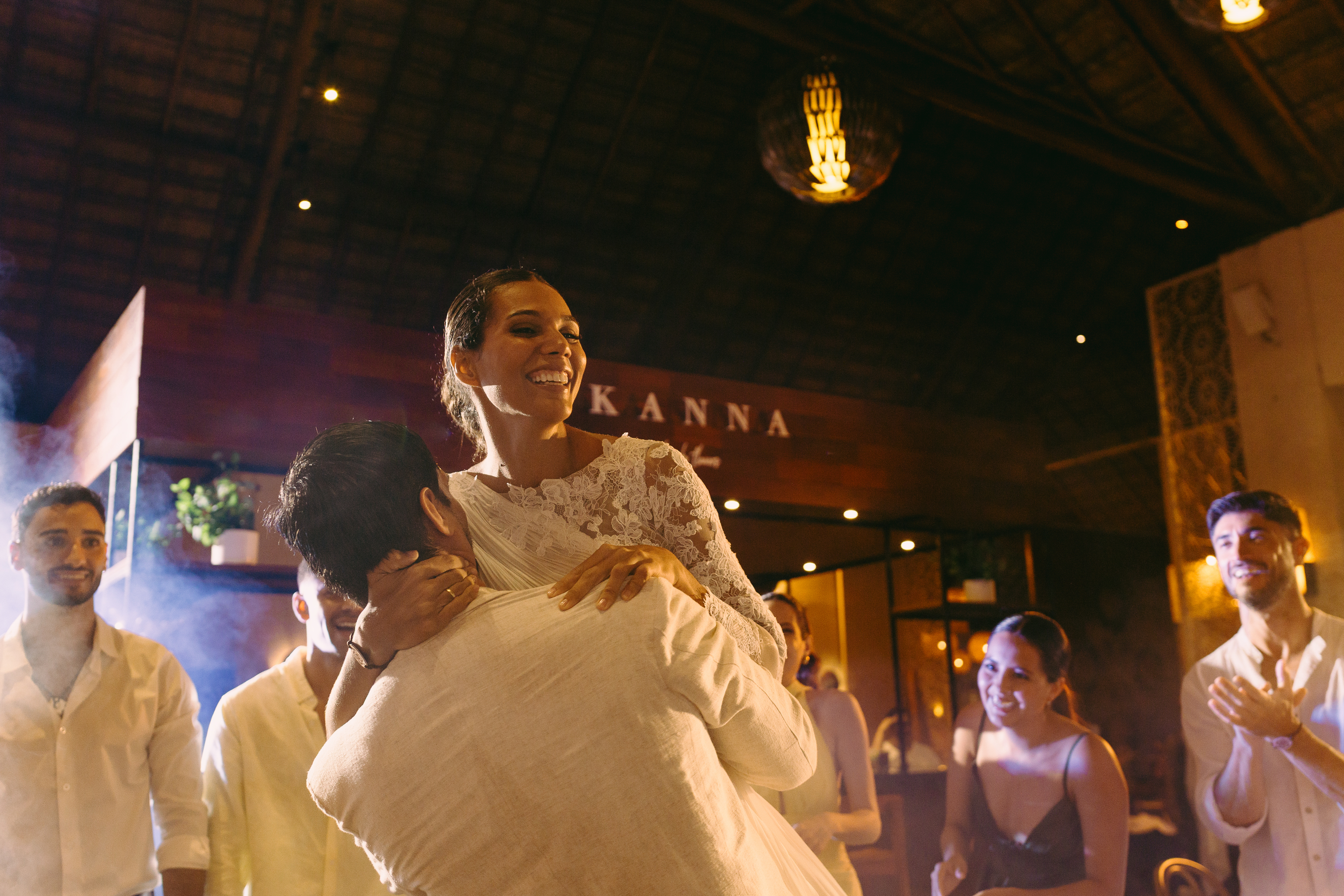 Bride in white lace dress lifted, dancing with groom at wedding reception.