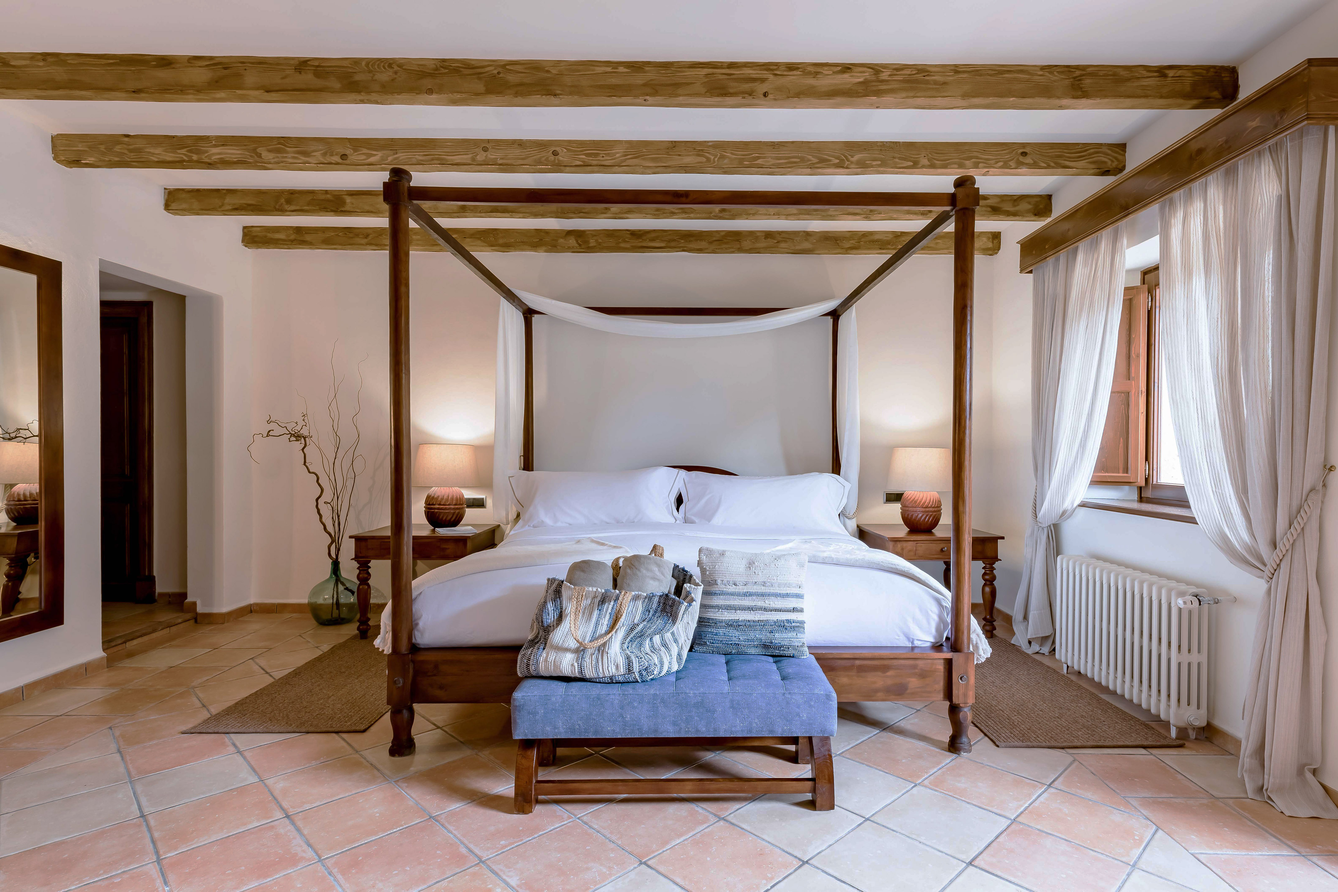 Rustic four-poster bedroom with wood beams, terracotta floor. Cozy hotel suite.