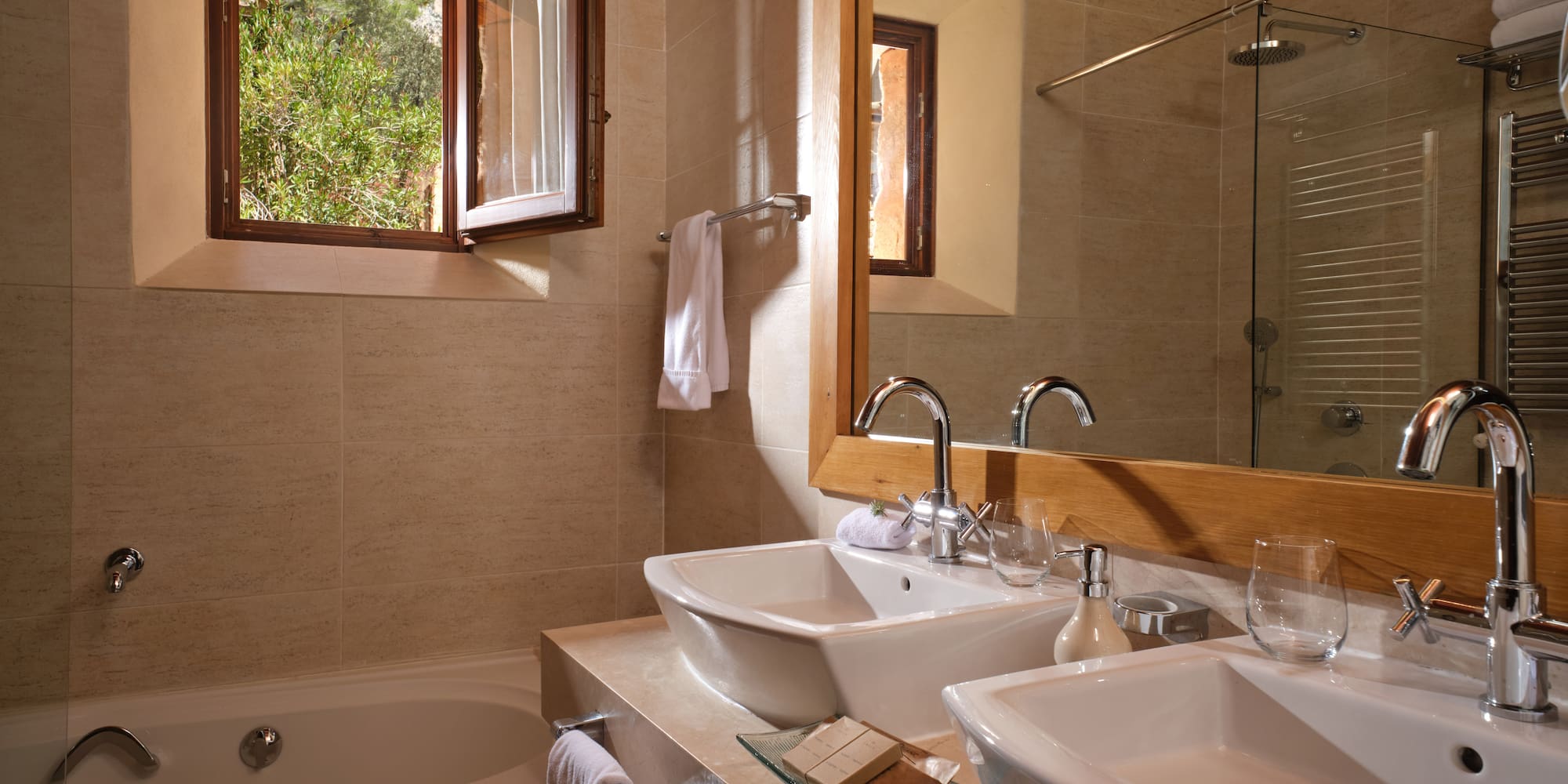 Modern bathroom with double vessel sinks, bathtub, and open window to greenery.
