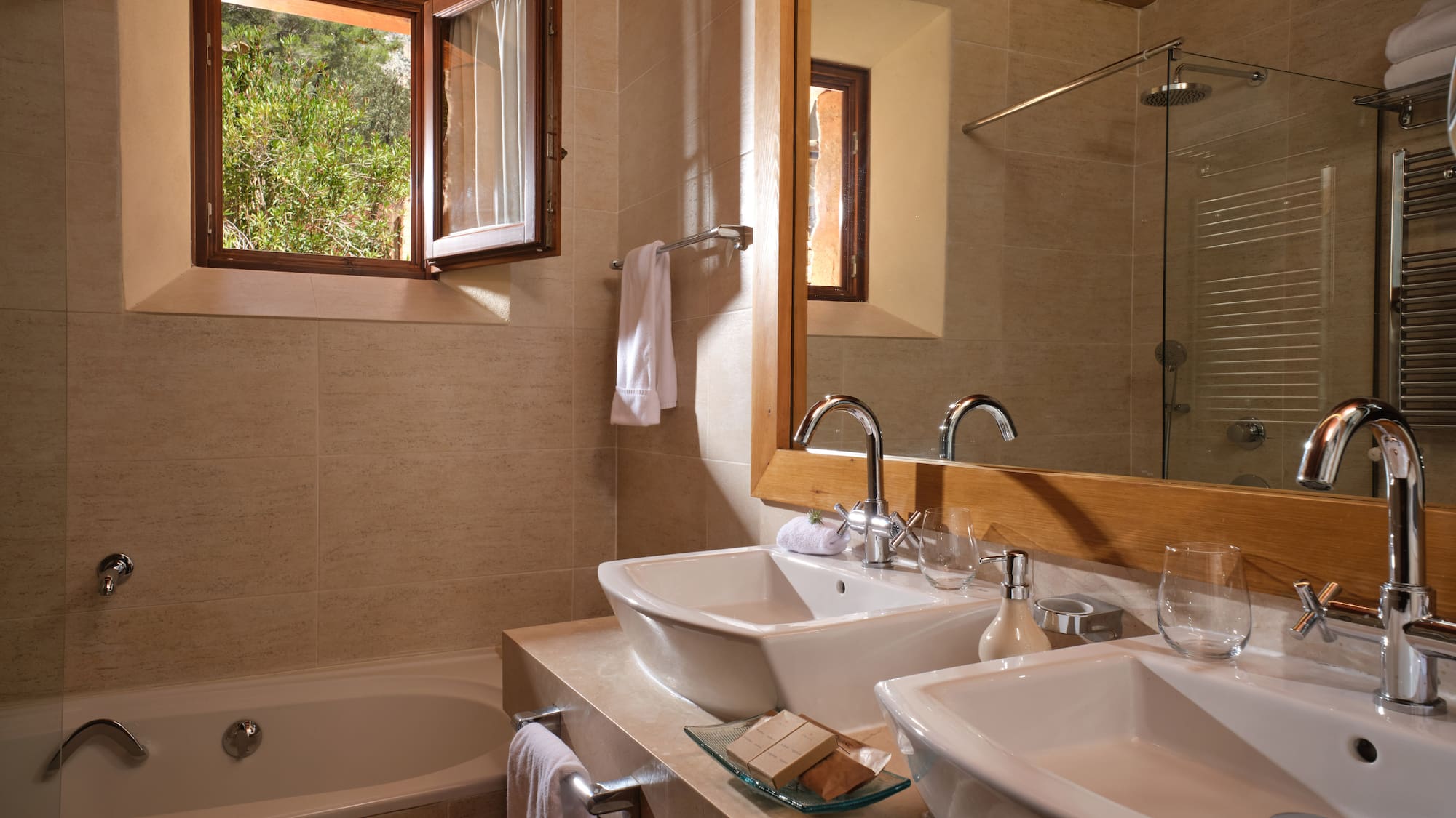 Modern bathroom with double vessel sinks, bathtub, and open window to greenery.