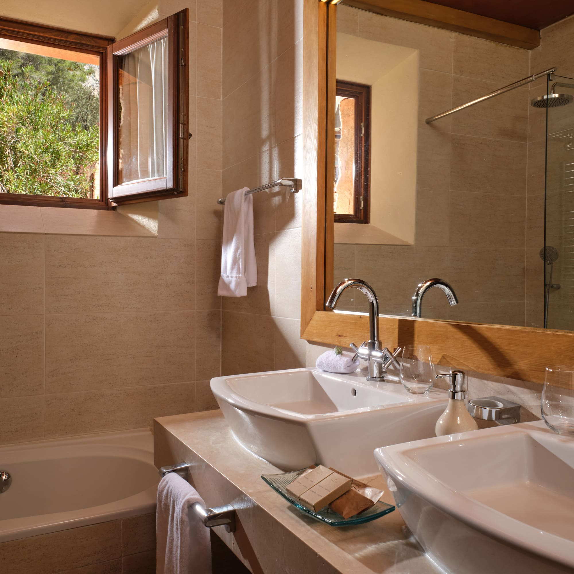 Modern bathroom with double vessel sinks, bathtub, and open window to greenery.