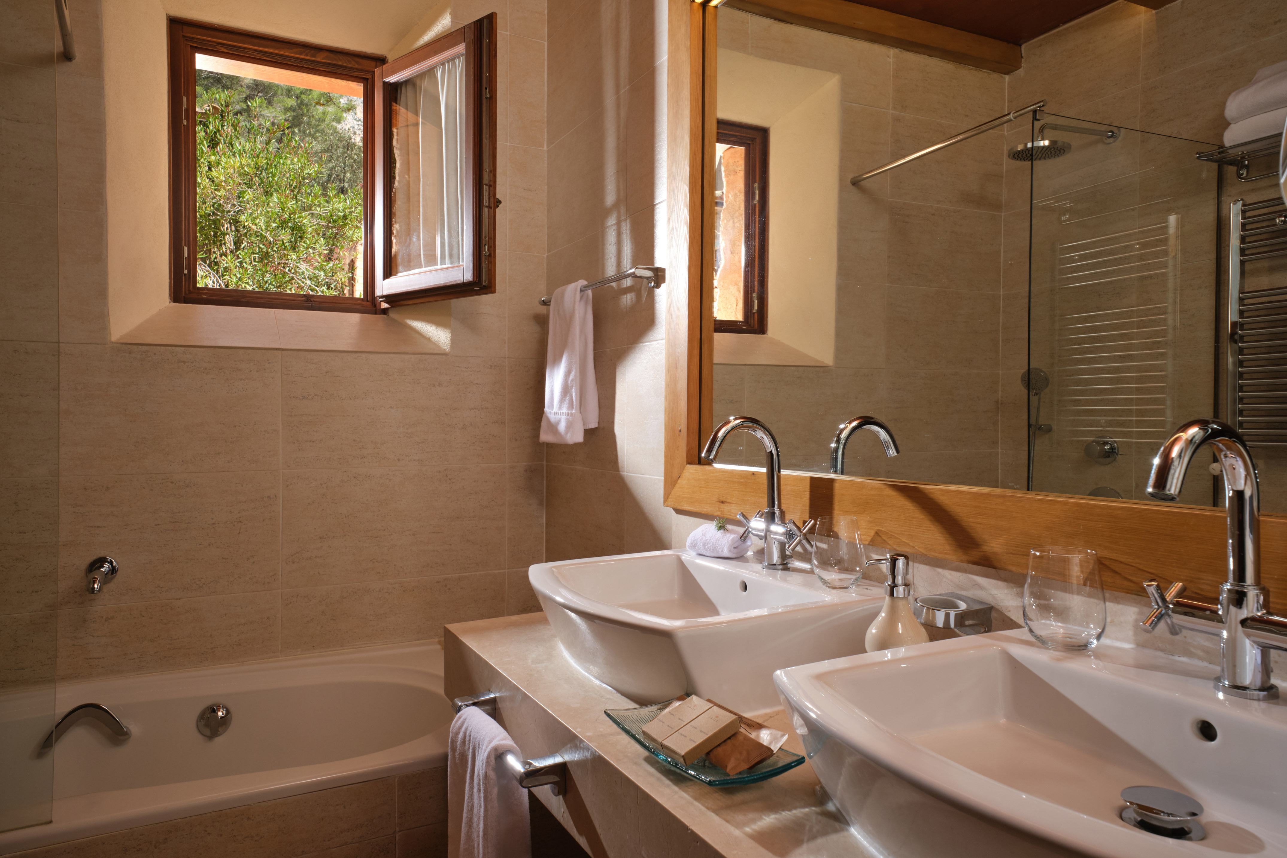 Modern bathroom with double vessel sinks, bathtub, and open window to greenery.