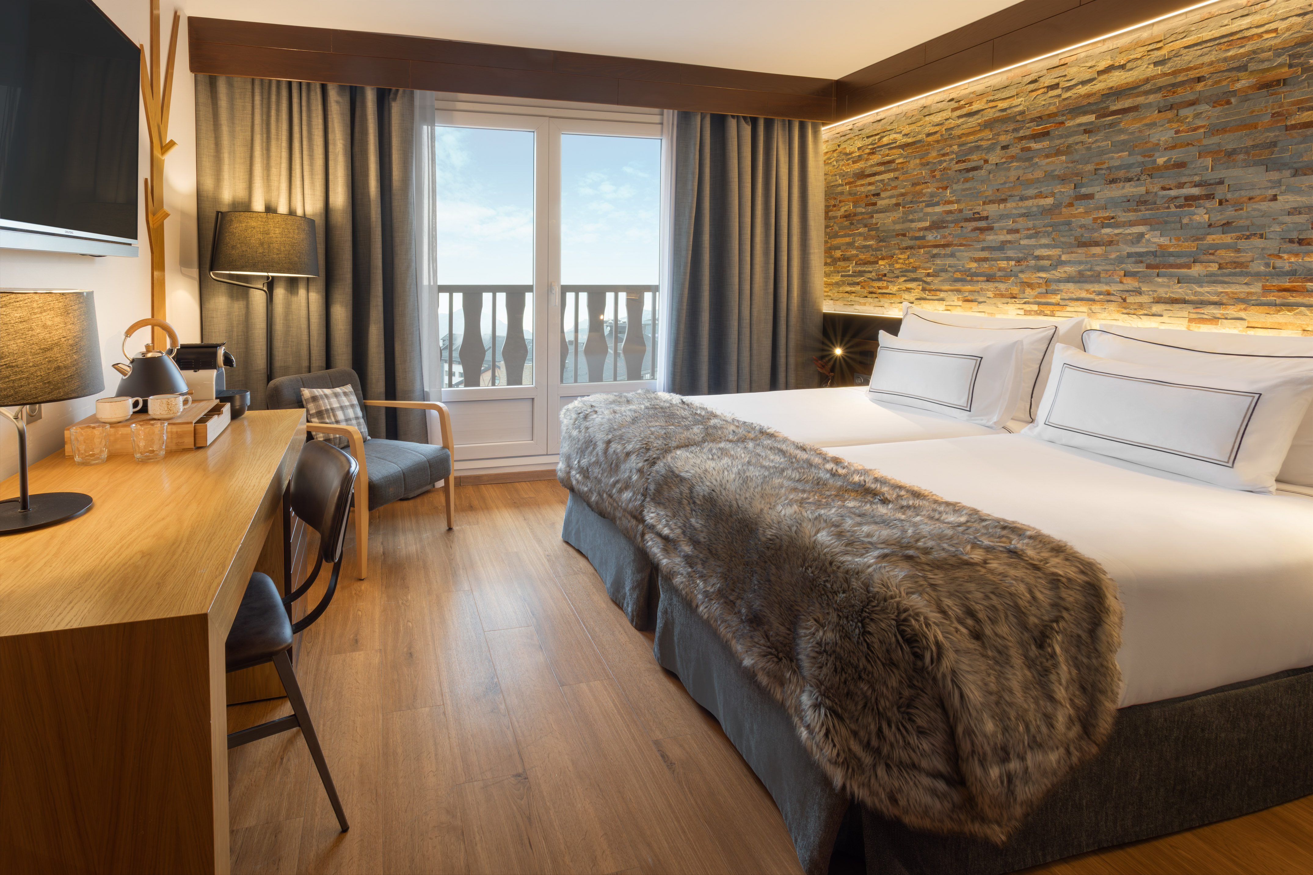 Stylish hotel bedroom with twin beds, stone wall, desk, and balcony access.