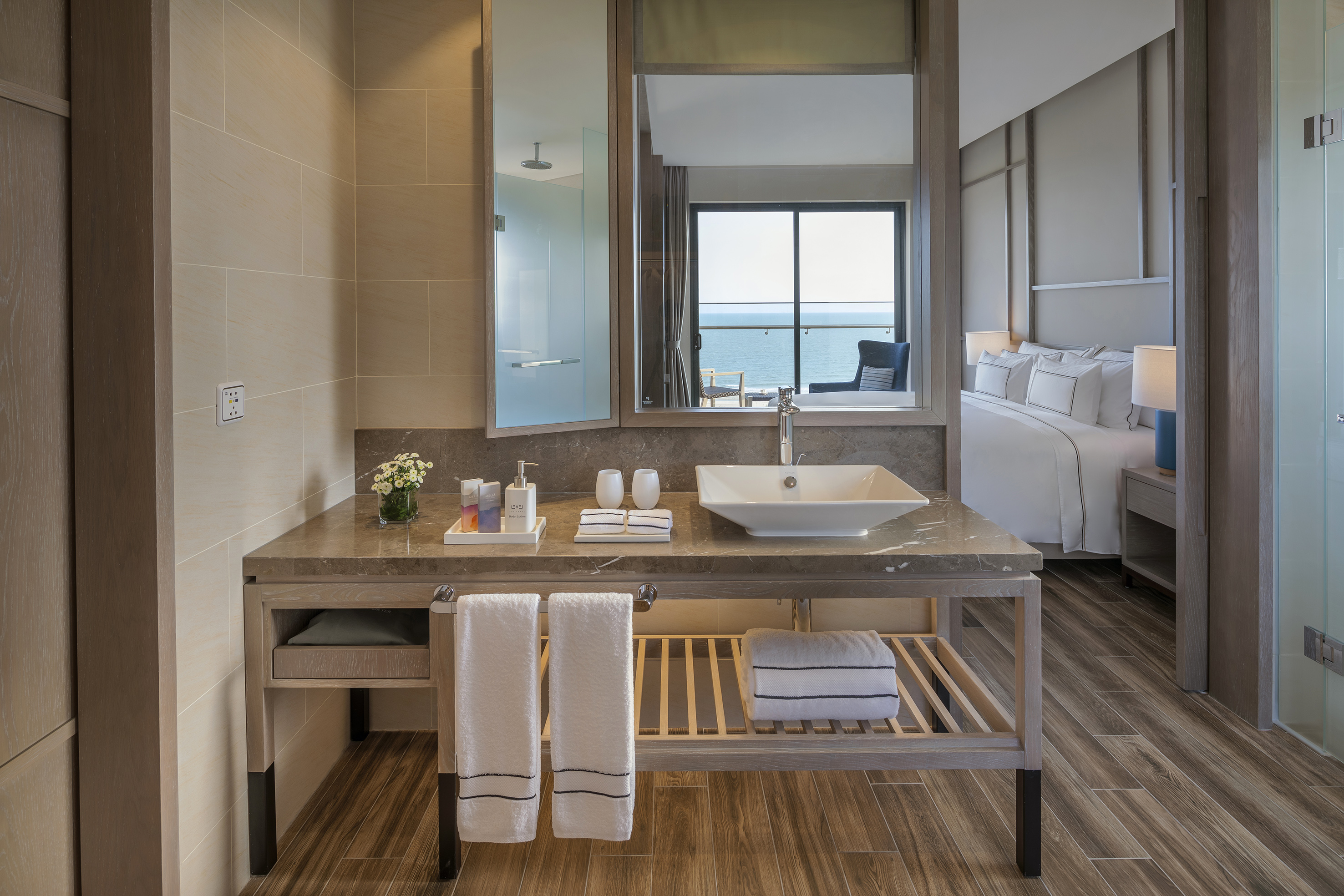Modern bathroom vanity, mirror reflects ocean view and luxury hotel bedroom.