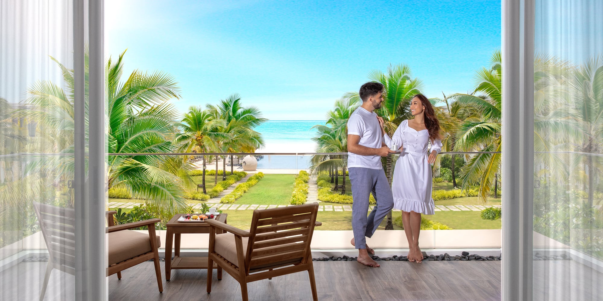 Couple on balcony overlooking tropical beach, ocean, and palm trees.