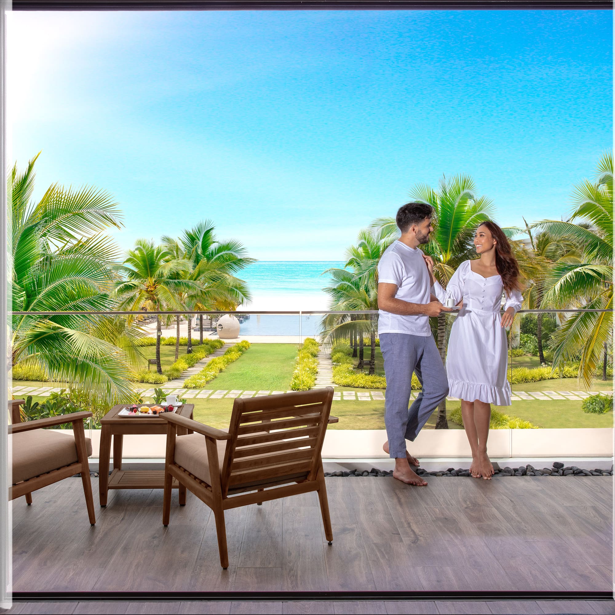 Couple on balcony overlooking tropical beach, ocean, and palm trees.