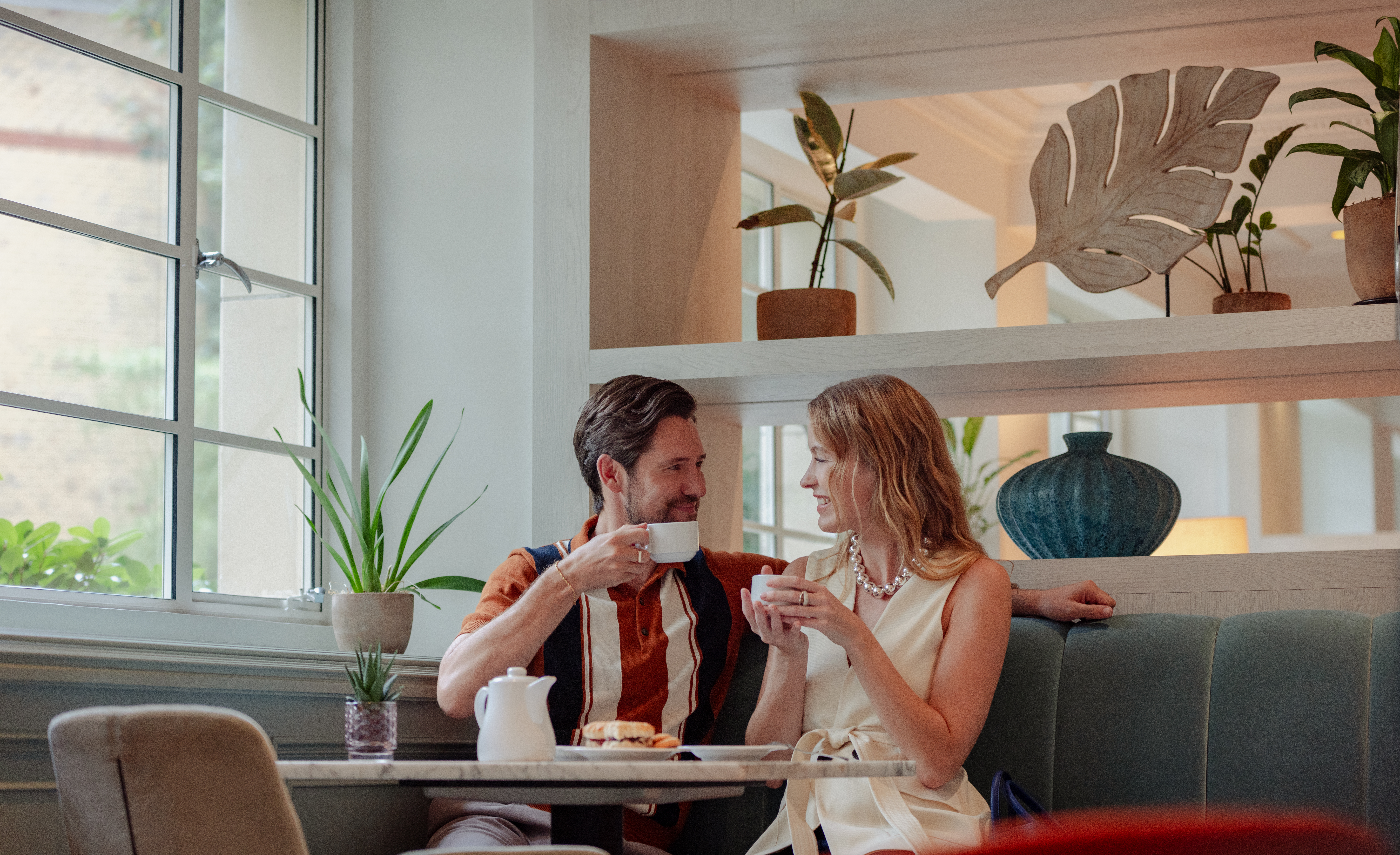 A man and a woman are seated at a table, each holding a coffee cup.