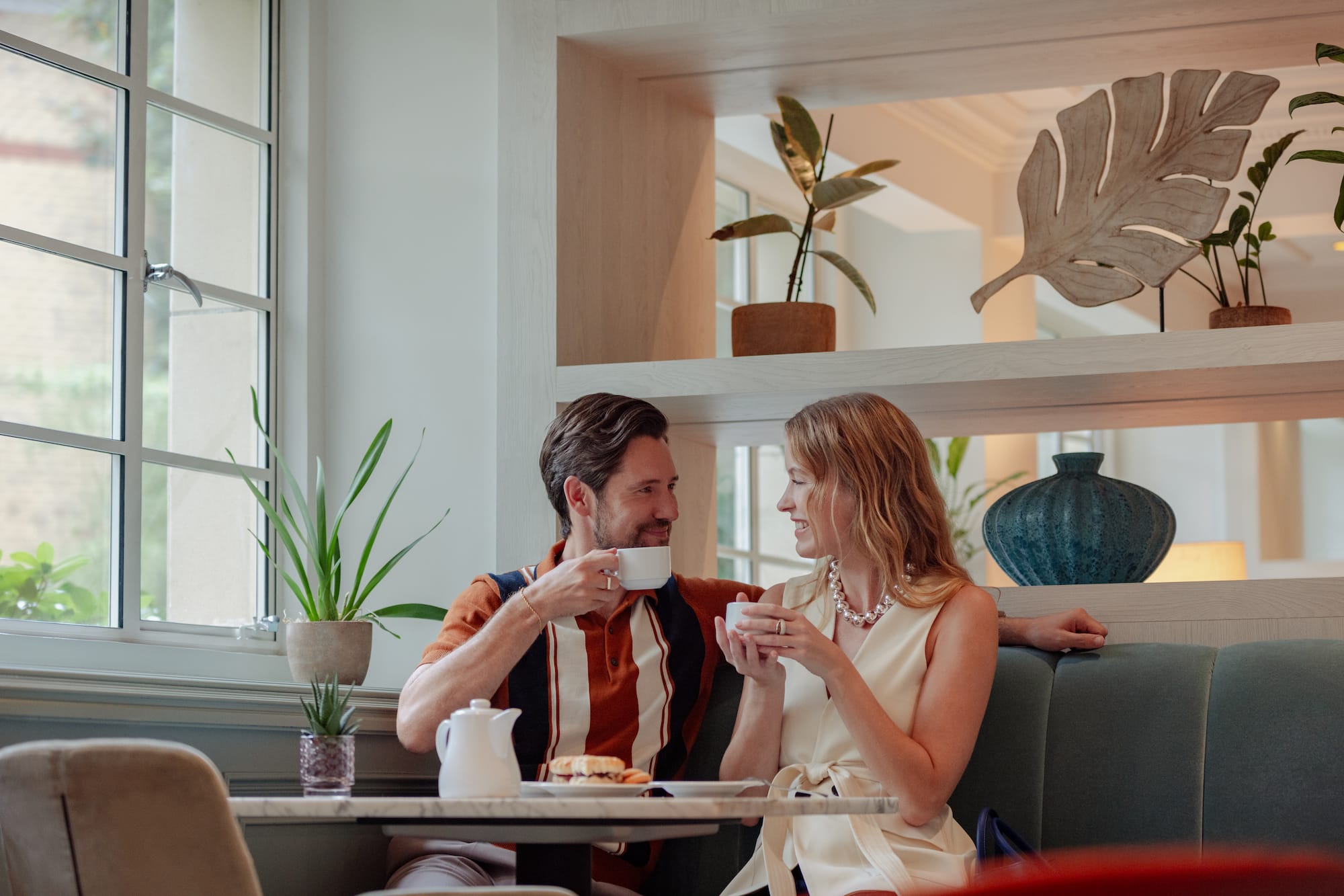 A man and a woman are seated at a table, each holding a coffee cup.