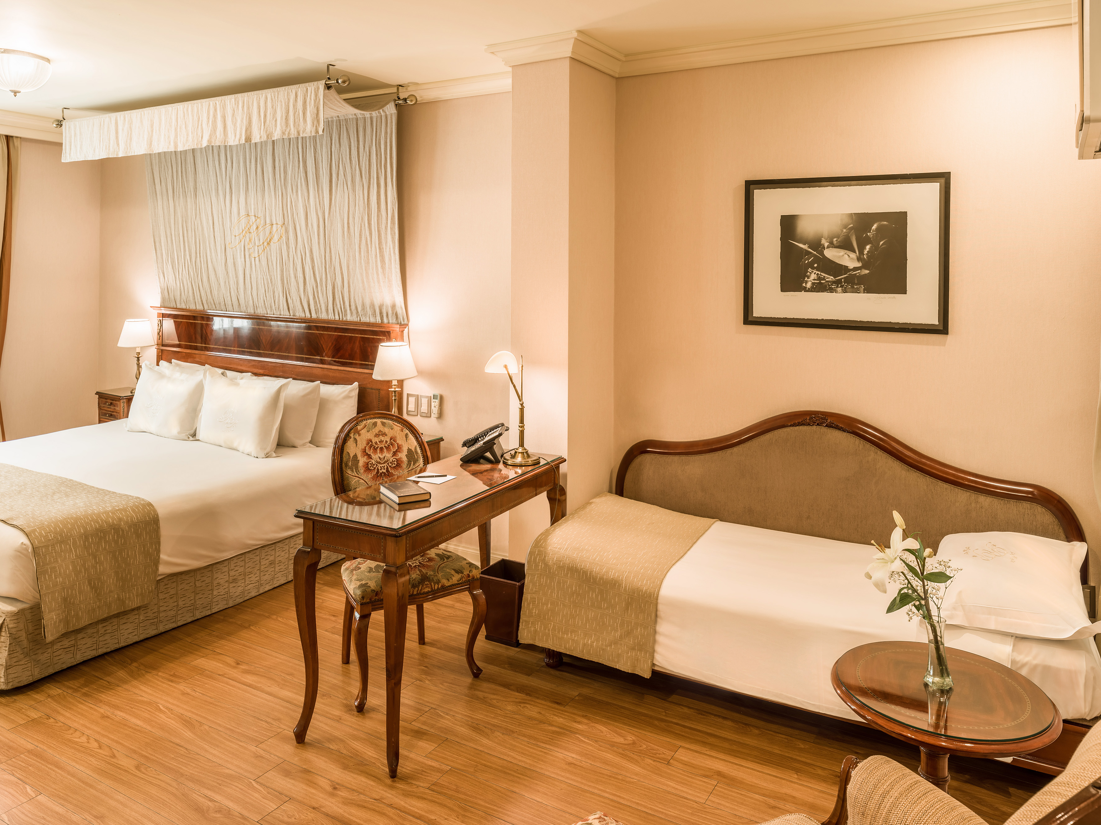 Elegant hotel room with queen bed, single bed, classic desk, and wood floor.