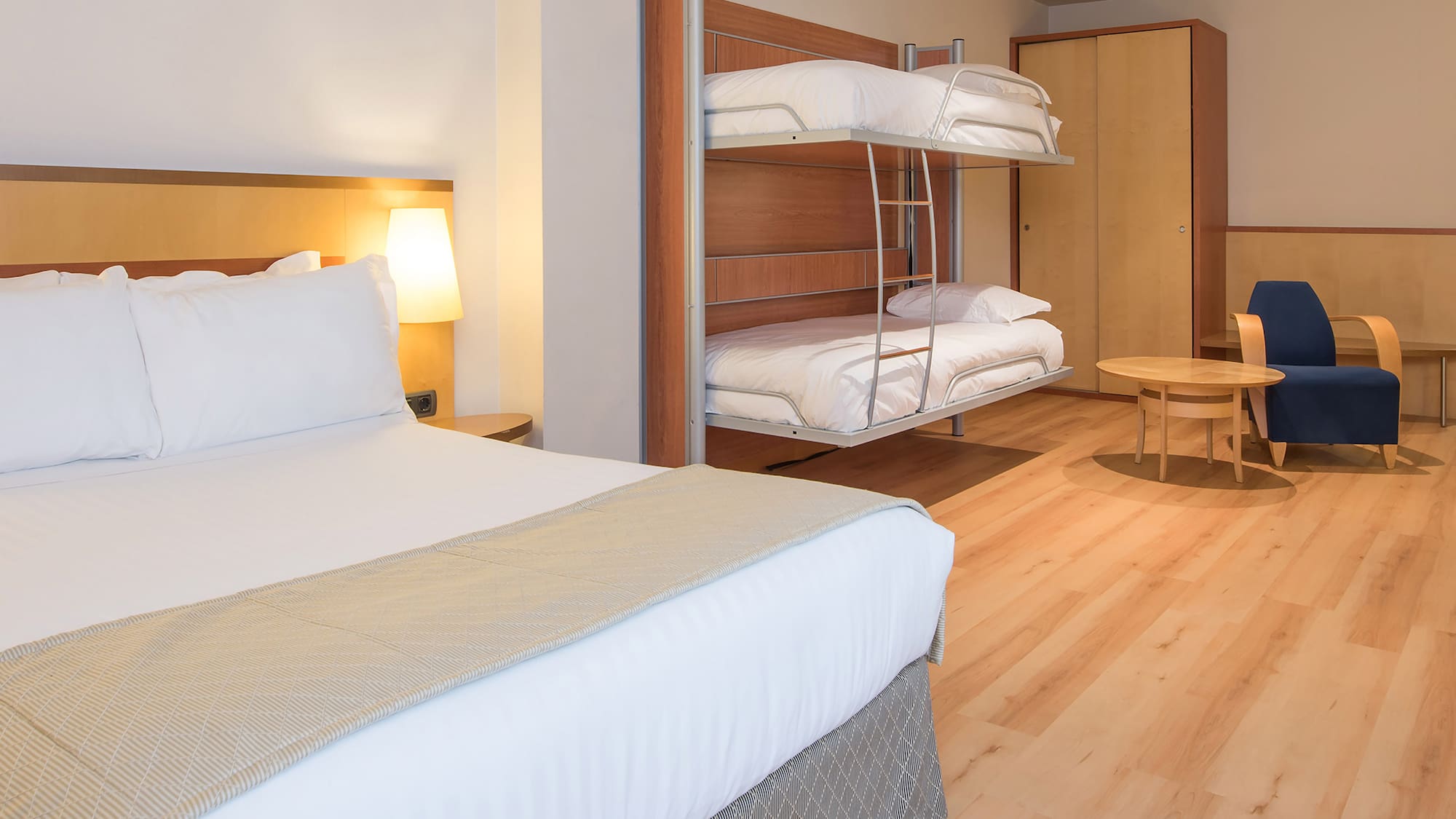 Spacious hotel family room with double bed and bunk beds on wooden floor.