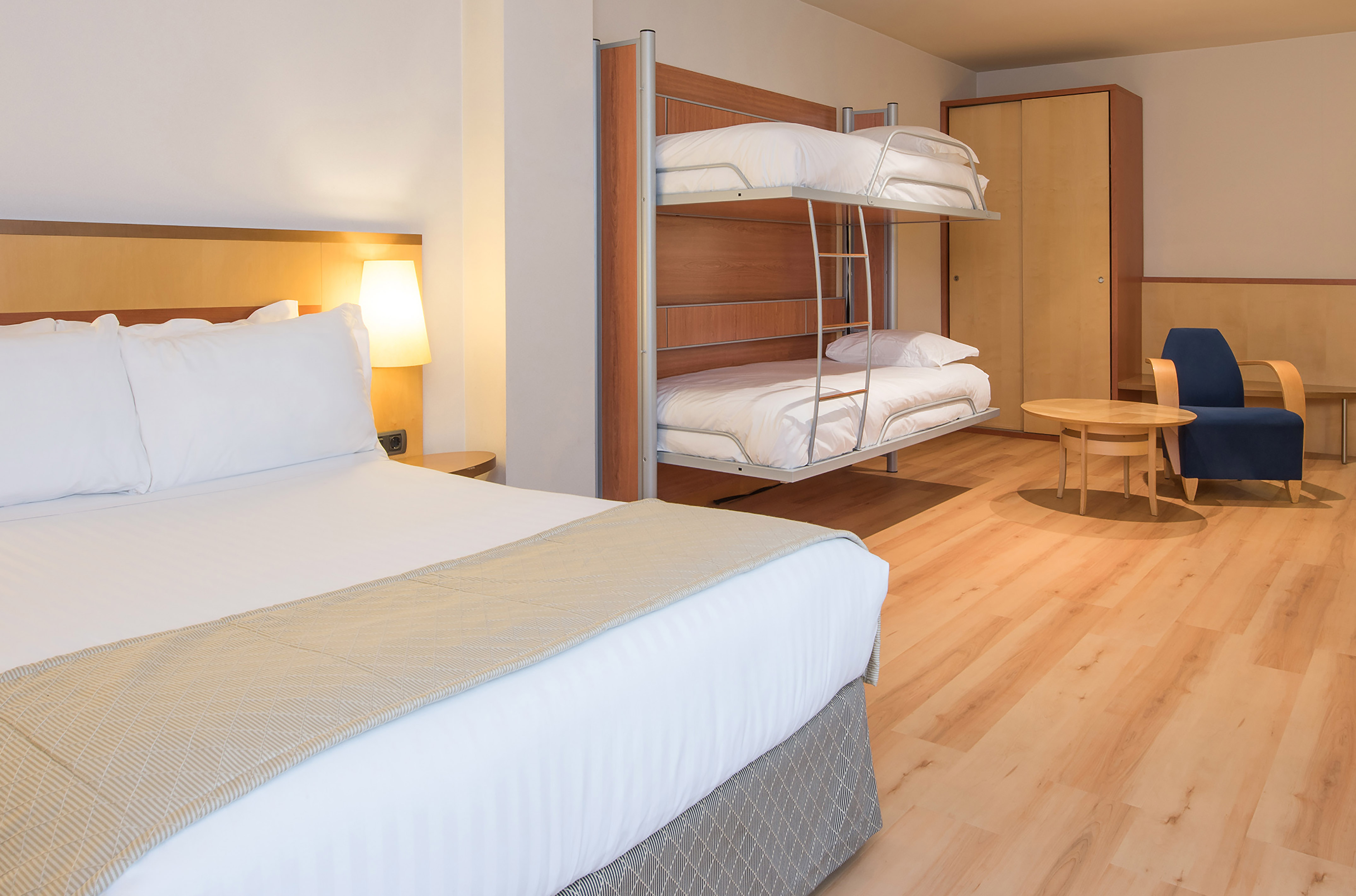 Spacious hotel family room with double bed and bunk beds on wooden floor.