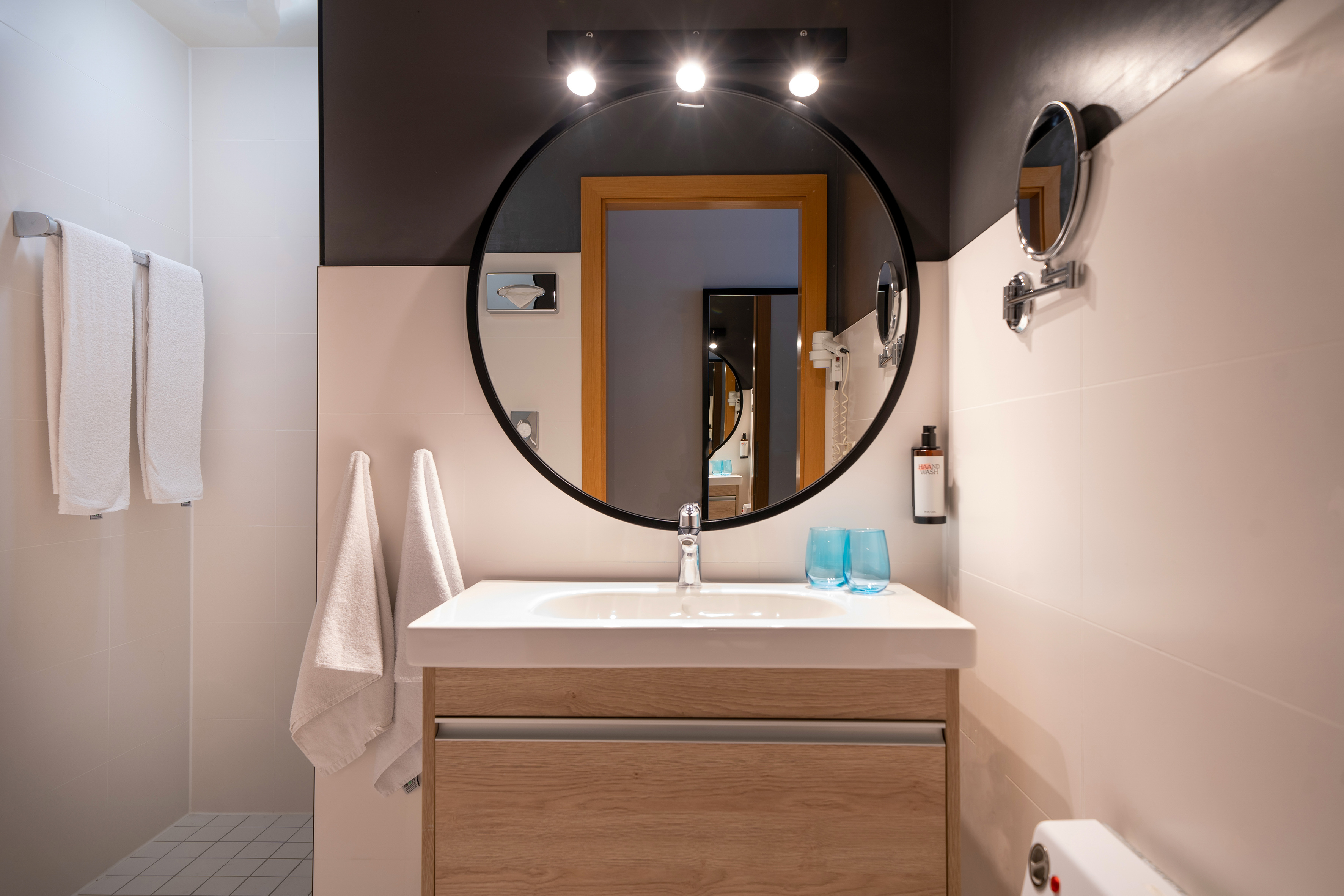 Modern bathroom with white sink vanity, round mirror, wooden cabinet, and towels.