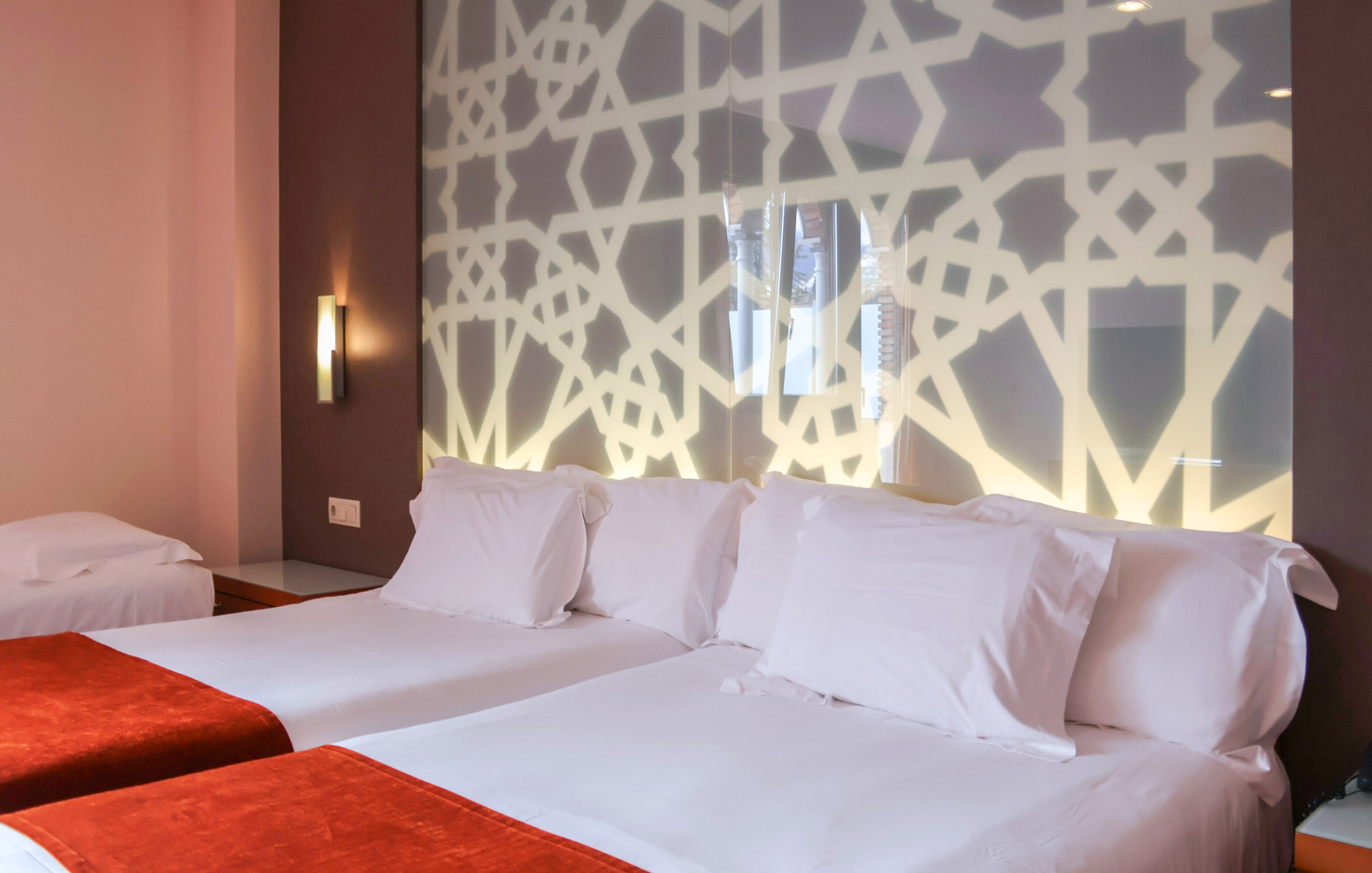 Twin hotel room with white beds, orange throws, and decorative geometric wall.