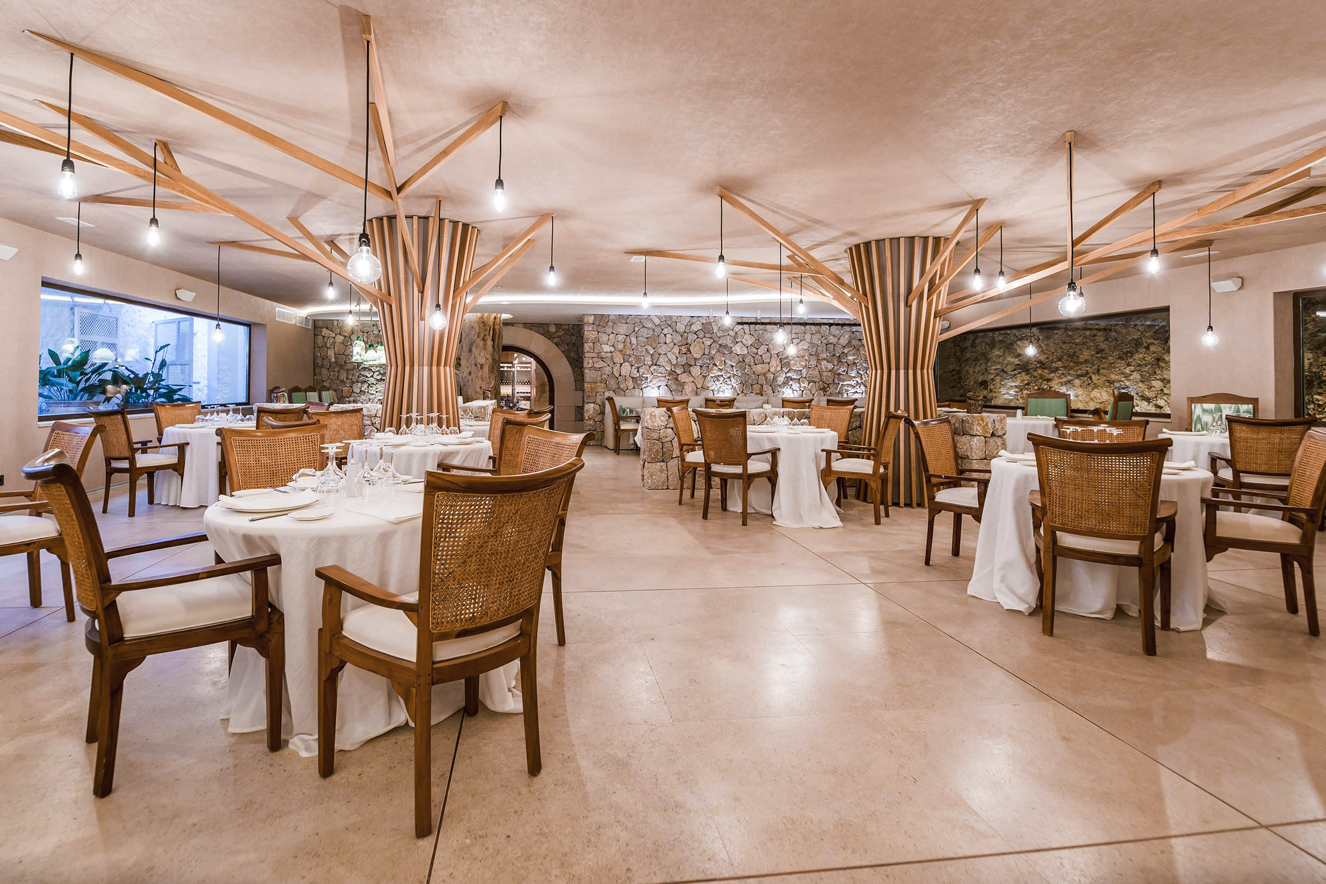 Elegant restaurant dining room with unique wooden ceiling, stone walls, and set tables.