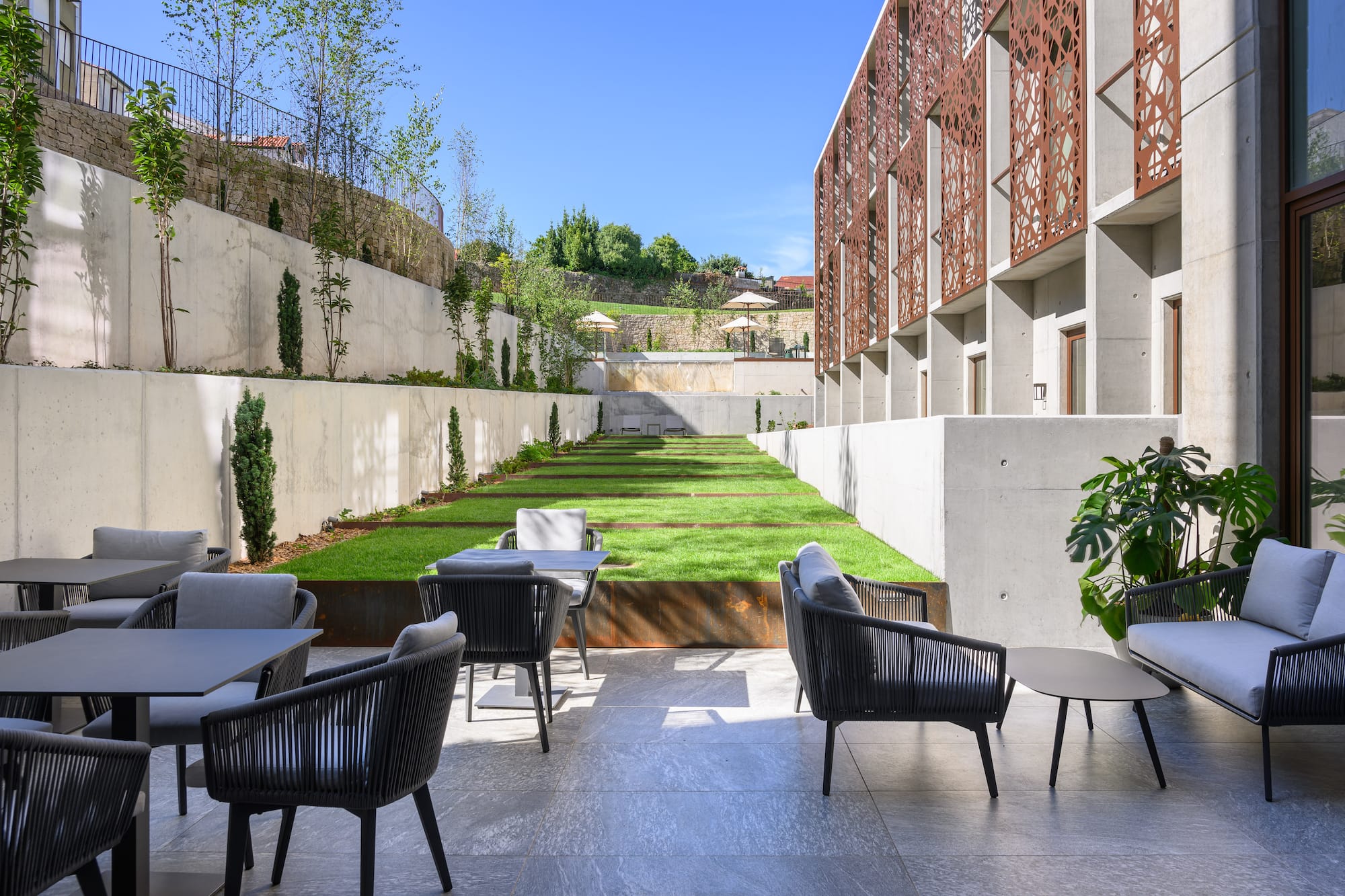 Outdoor lounge patio with terraced garden and modern building with screens.
