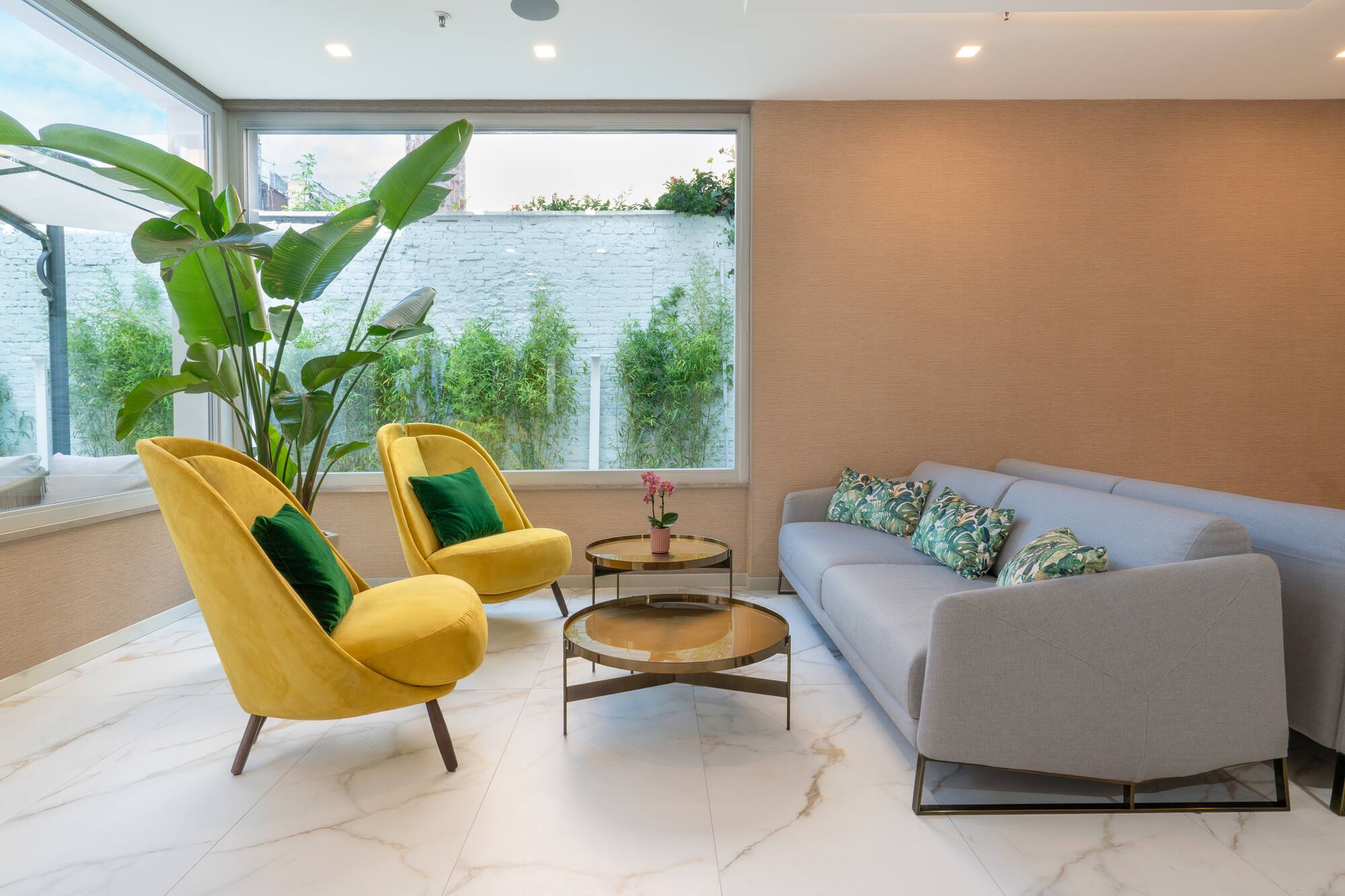 Modern lounge with yellow armchairs, grey sofa, marble floor, and tropical plants.