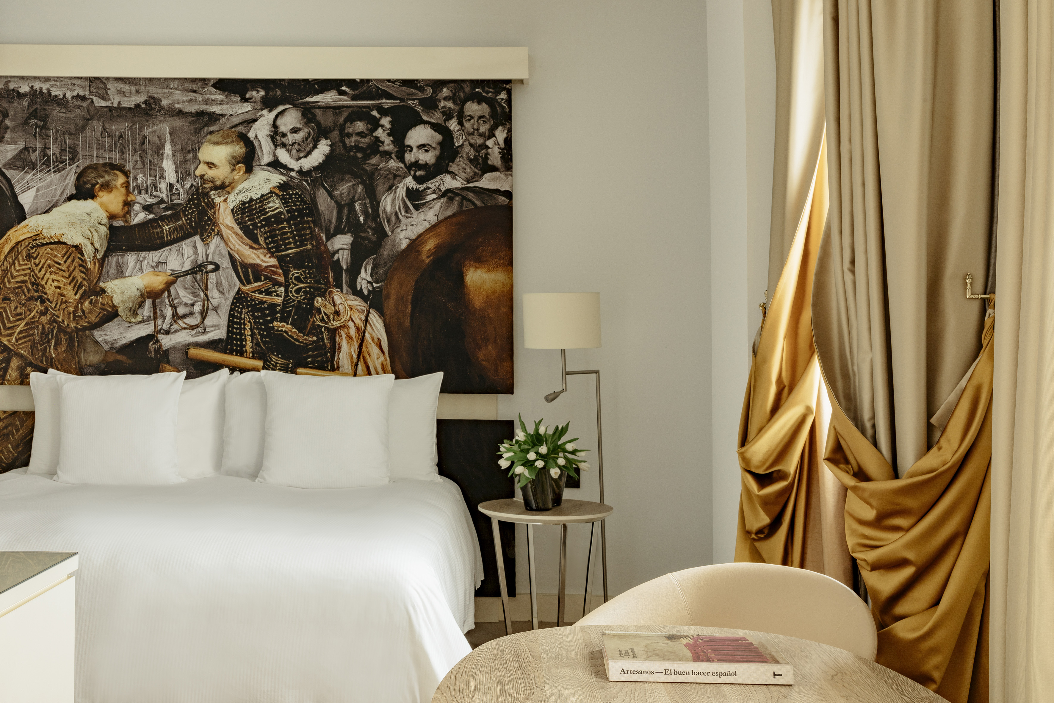 Luxurious hotel room with a white bed, Velázquez painting mural, and gold curtains.