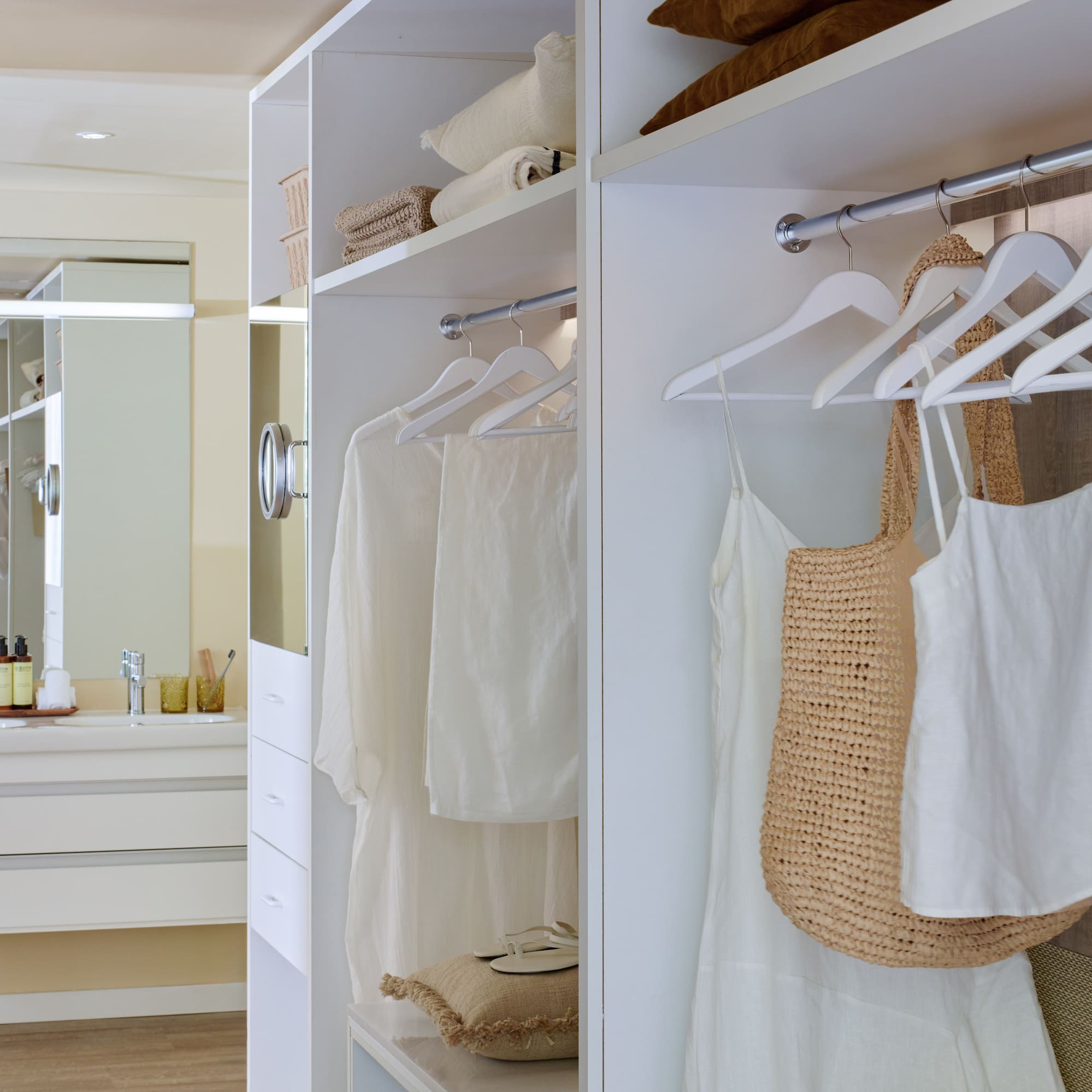 White walk-in closet with organized clothes next to a modern bathroom vanity.