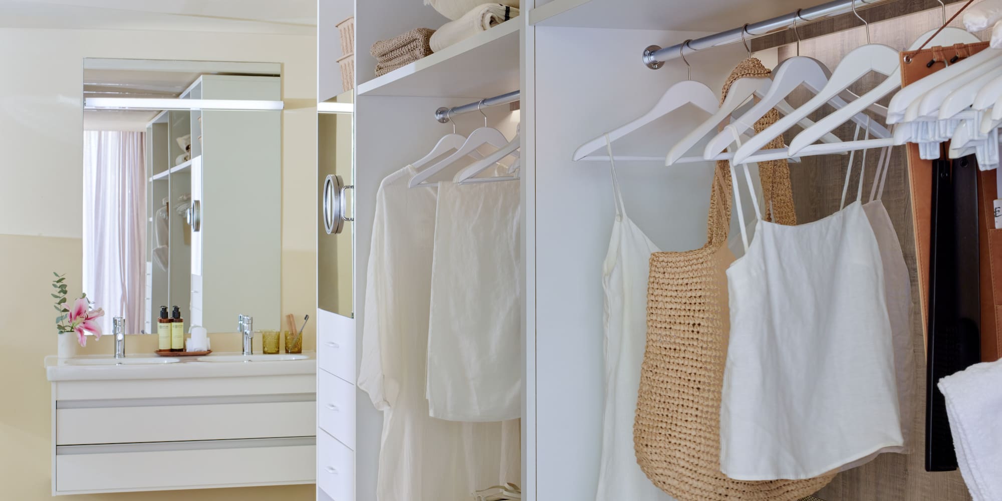White walk-in closet with organized clothes next to a modern bathroom vanity.