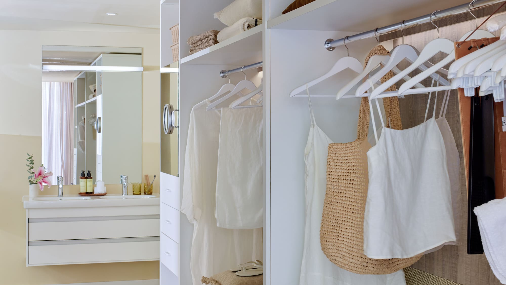 White walk-in closet with organized clothes next to a modern bathroom vanity.