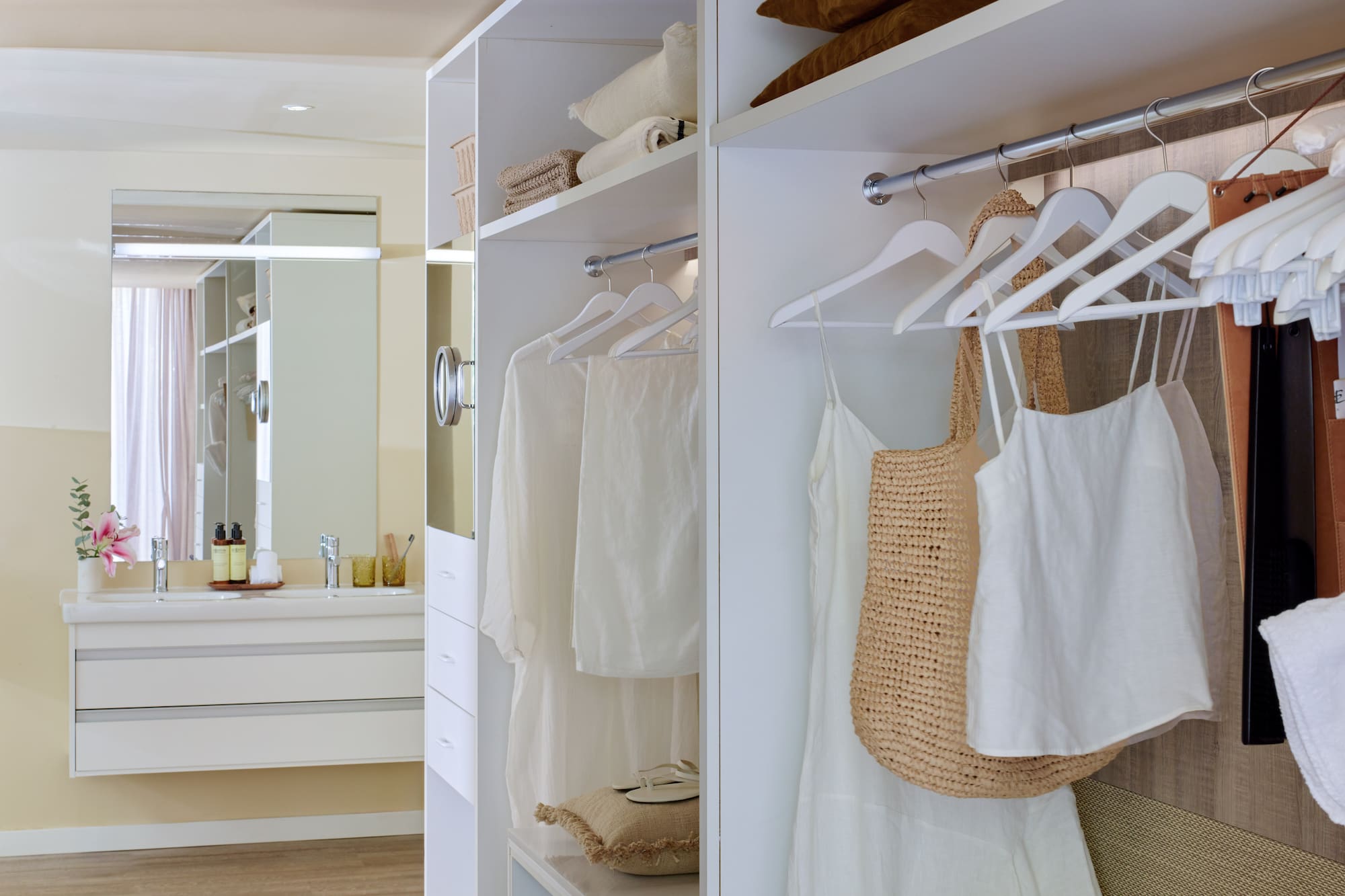 White walk-in closet with organized clothes next to a modern bathroom vanity.