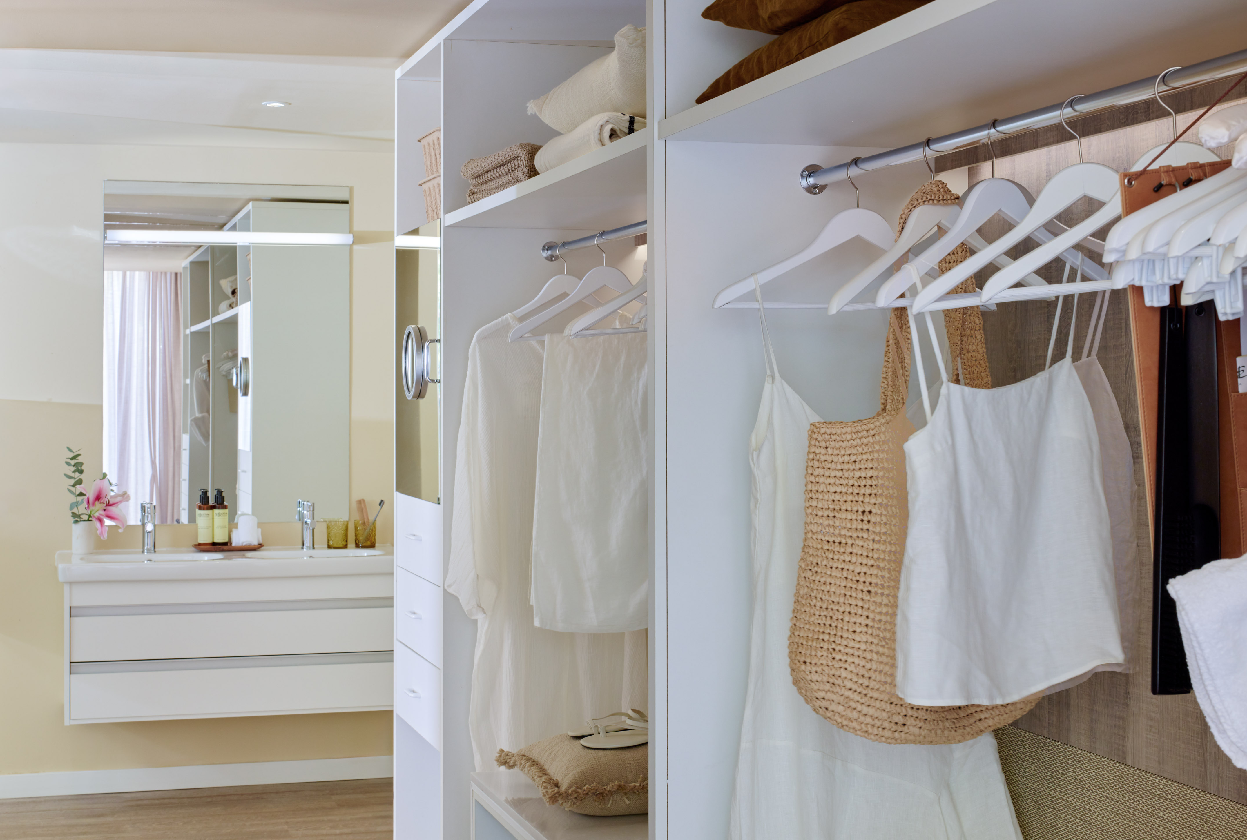 White walk-in closet with organized clothes next to a modern bathroom vanity.