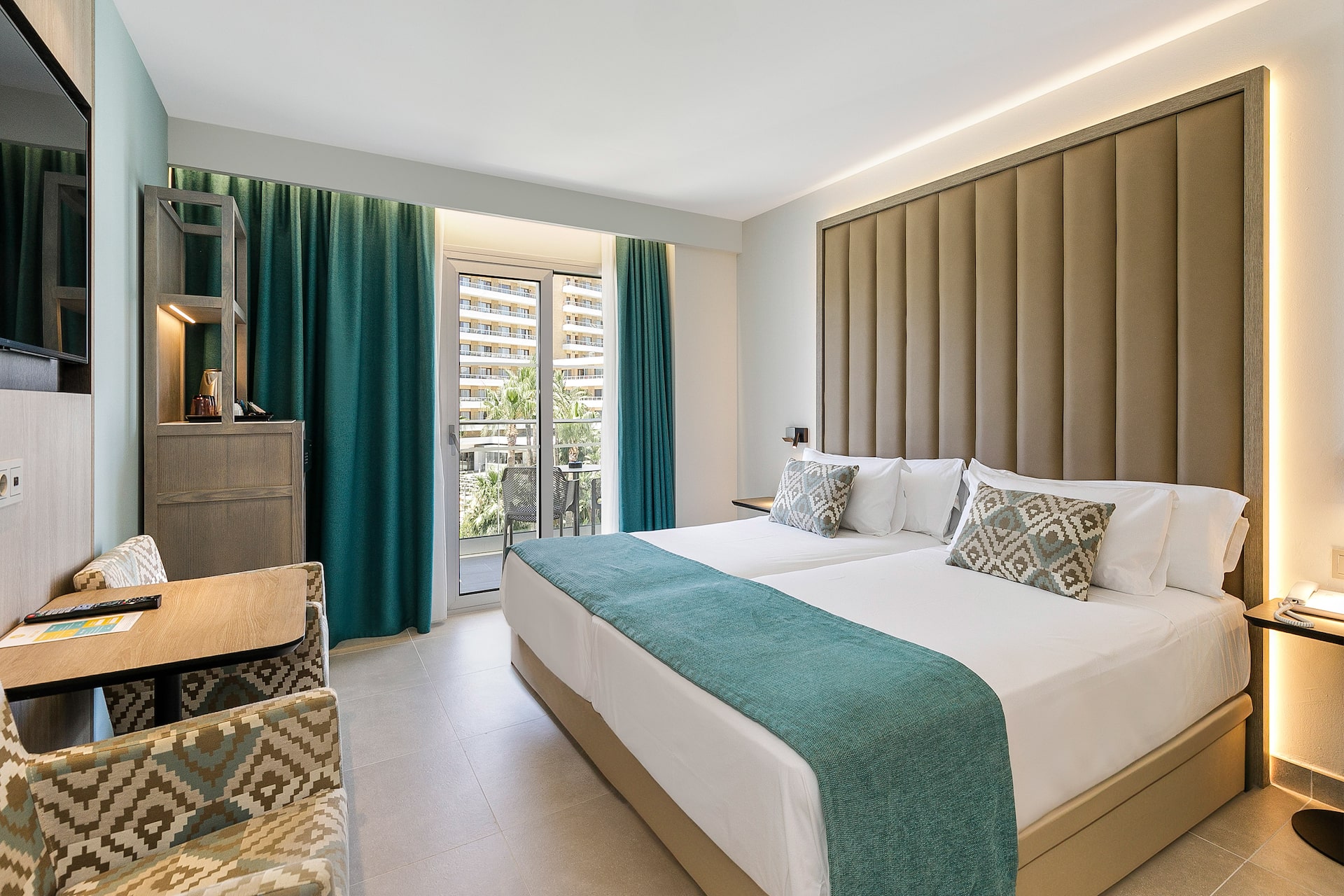 Modern hotel room with twin beds, teal accents, and a balcony view.