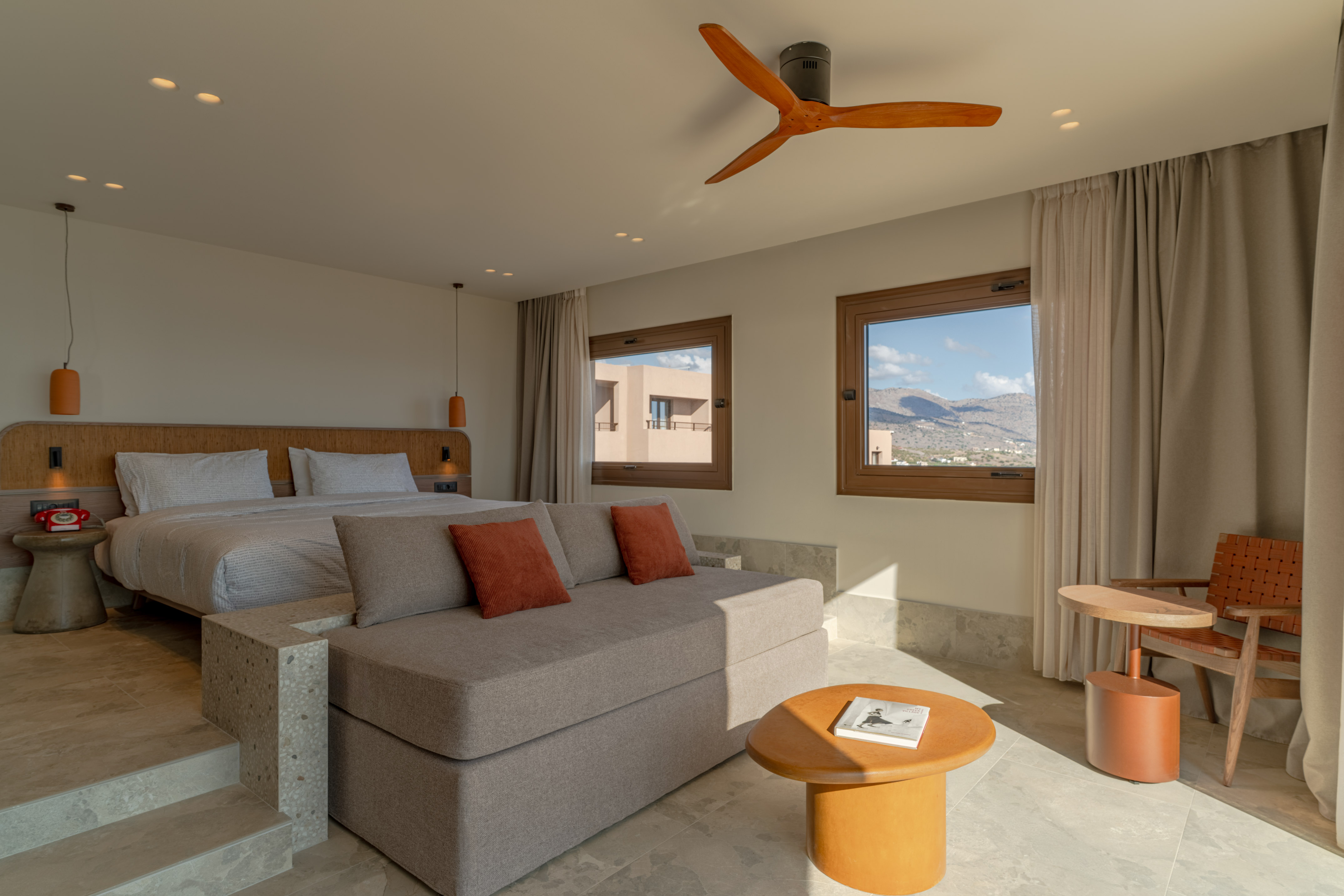 Modern hotel bedroom with king bed, grey sofa, and scenic mountain views.