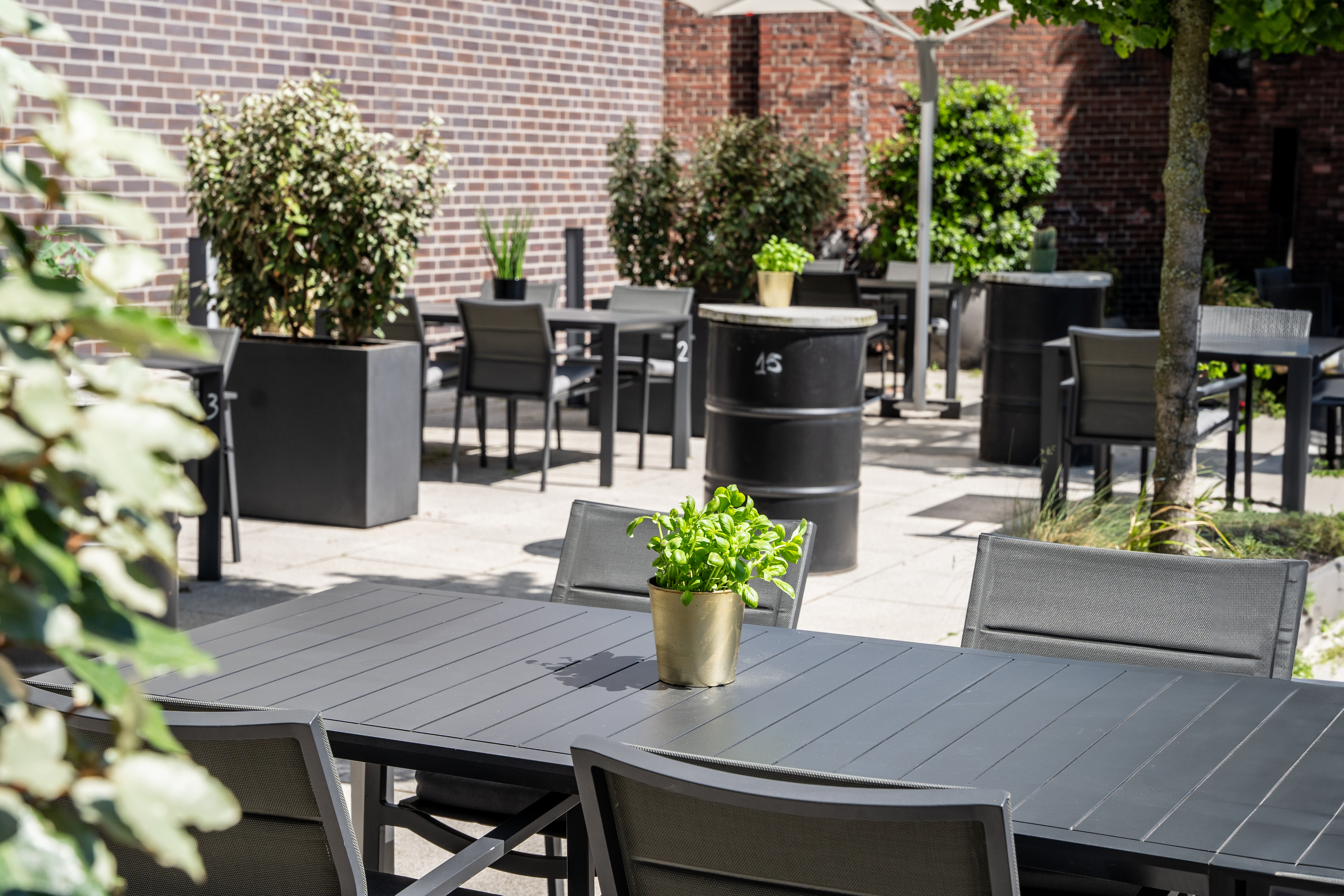 Outdoor restaurant patio with dark grey tables, chairs, and potted greenery.